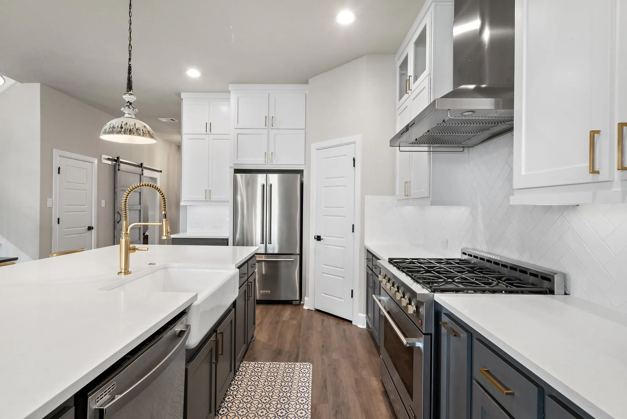White shaker cabinetry, stainless steel appliances, wood-finish flooring, quartz countertops, and a herringbone tile backsplash