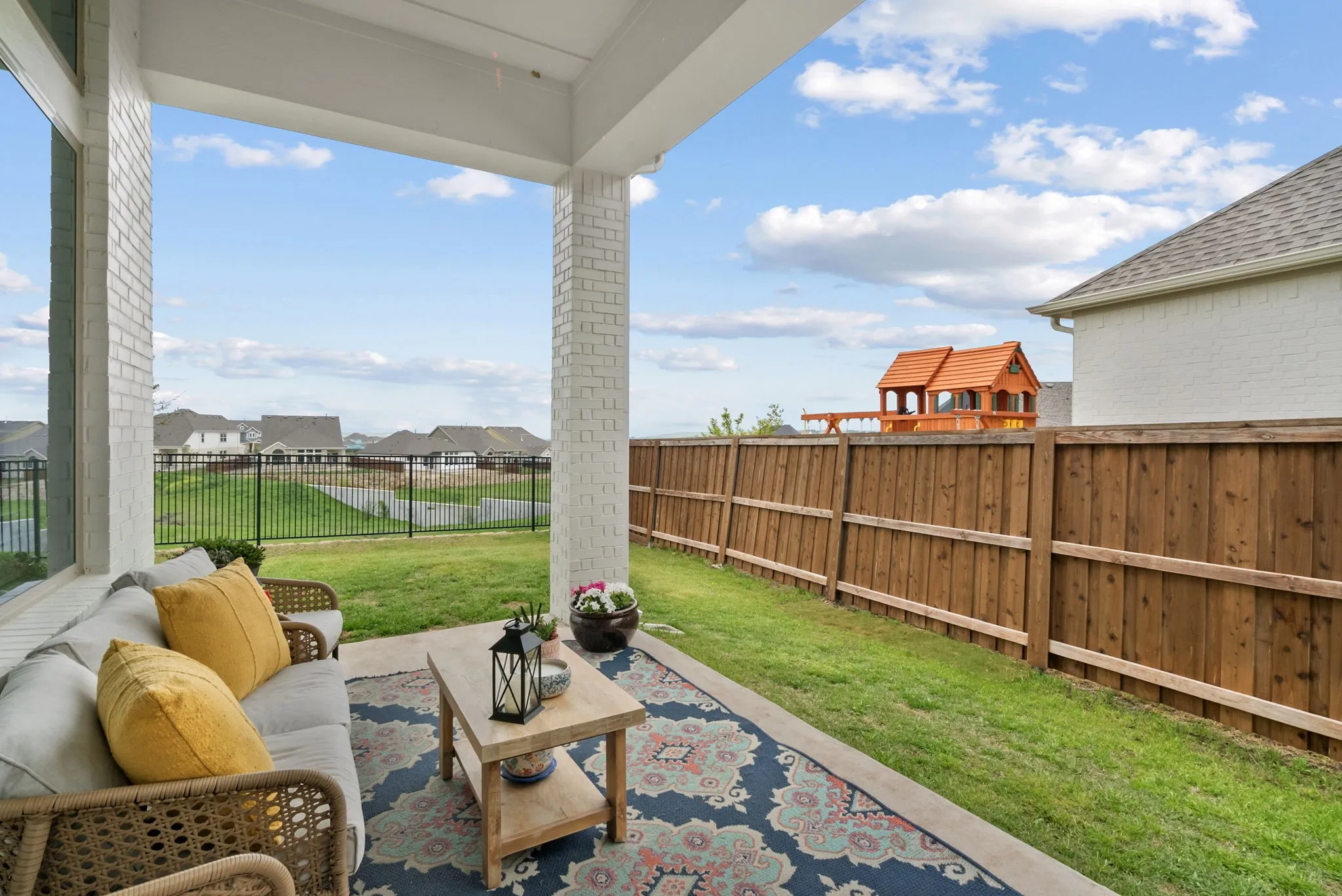 Covered patio with white brick columns, concrete flooring, and a wood privacy fence