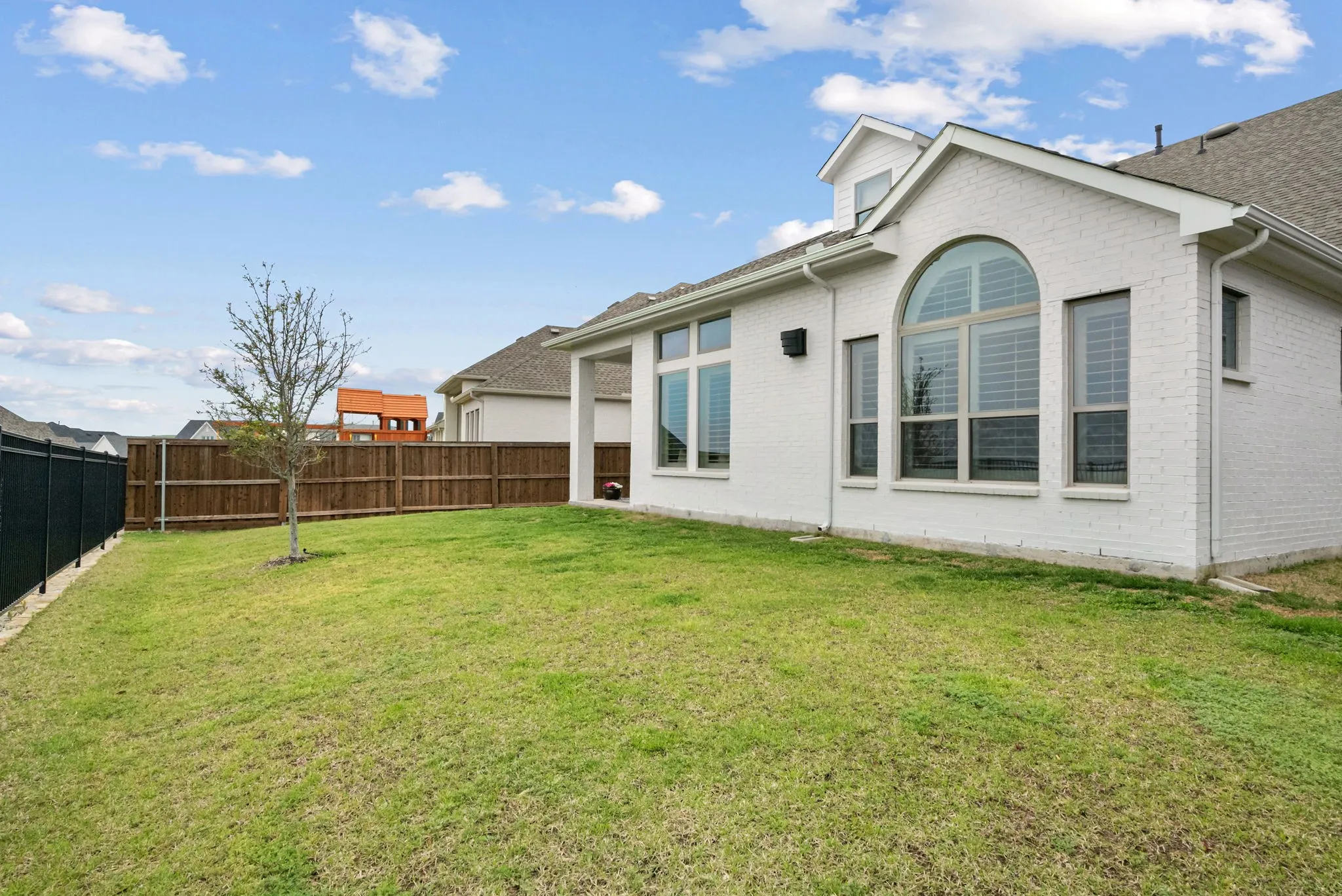 Expansive green lawn with a wood privacy fence and black metal fencing