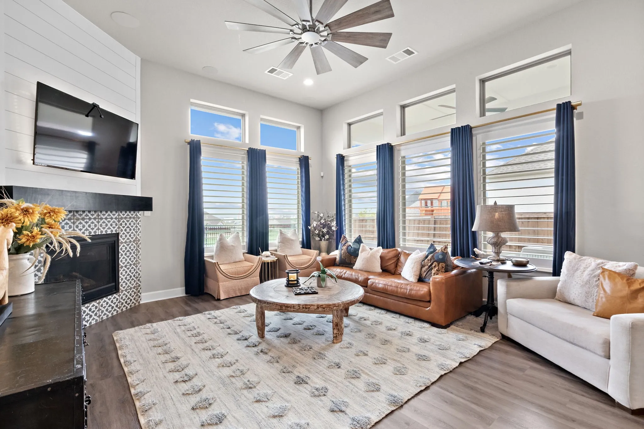 Vaulted ceiling with a large ceiling fan, fireplace with patterned tile surround, wood-finish flooring, and multiple windows