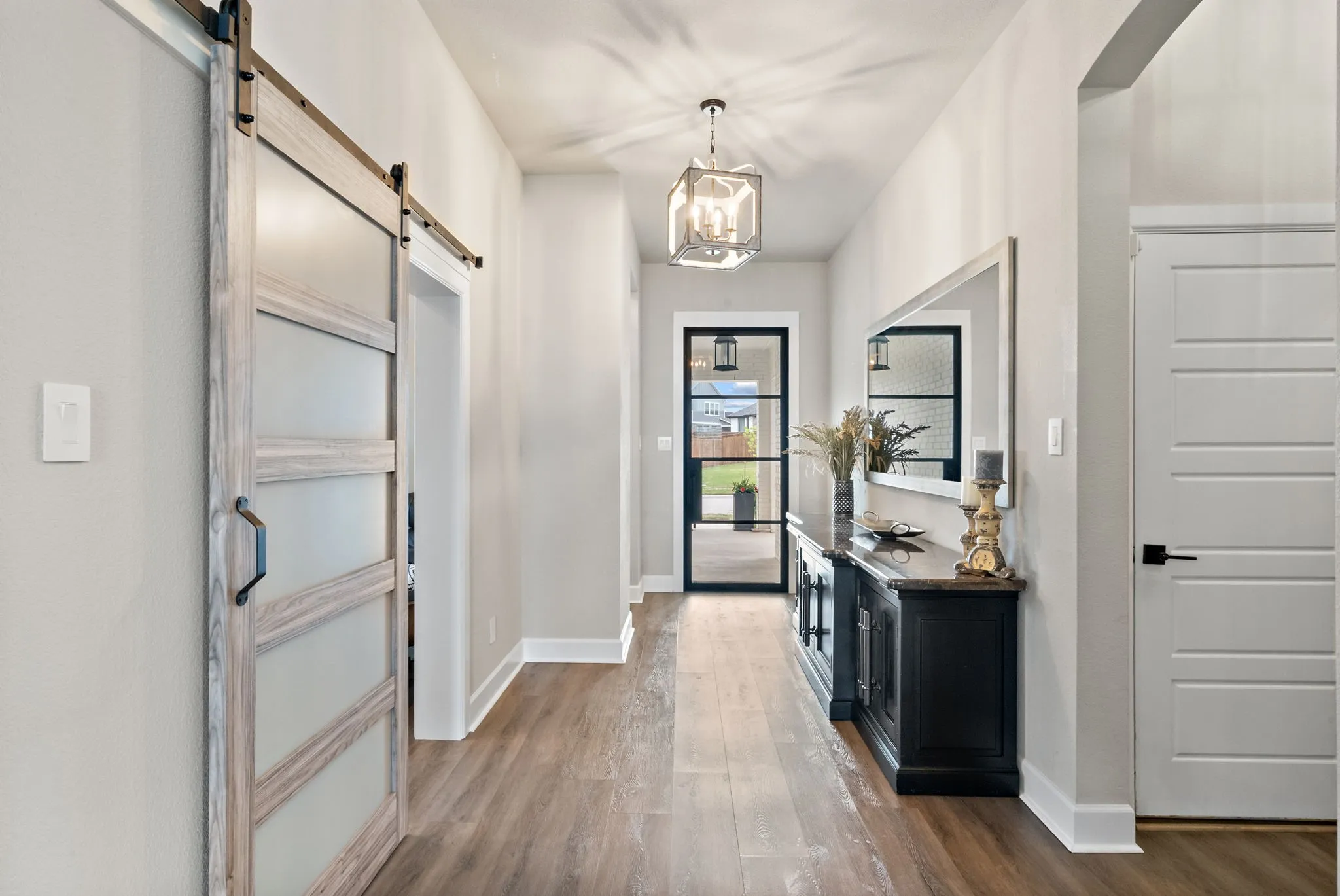 Wood-finish flooring, white paneled interior doors, and a wood-finish barn door with frosted panels