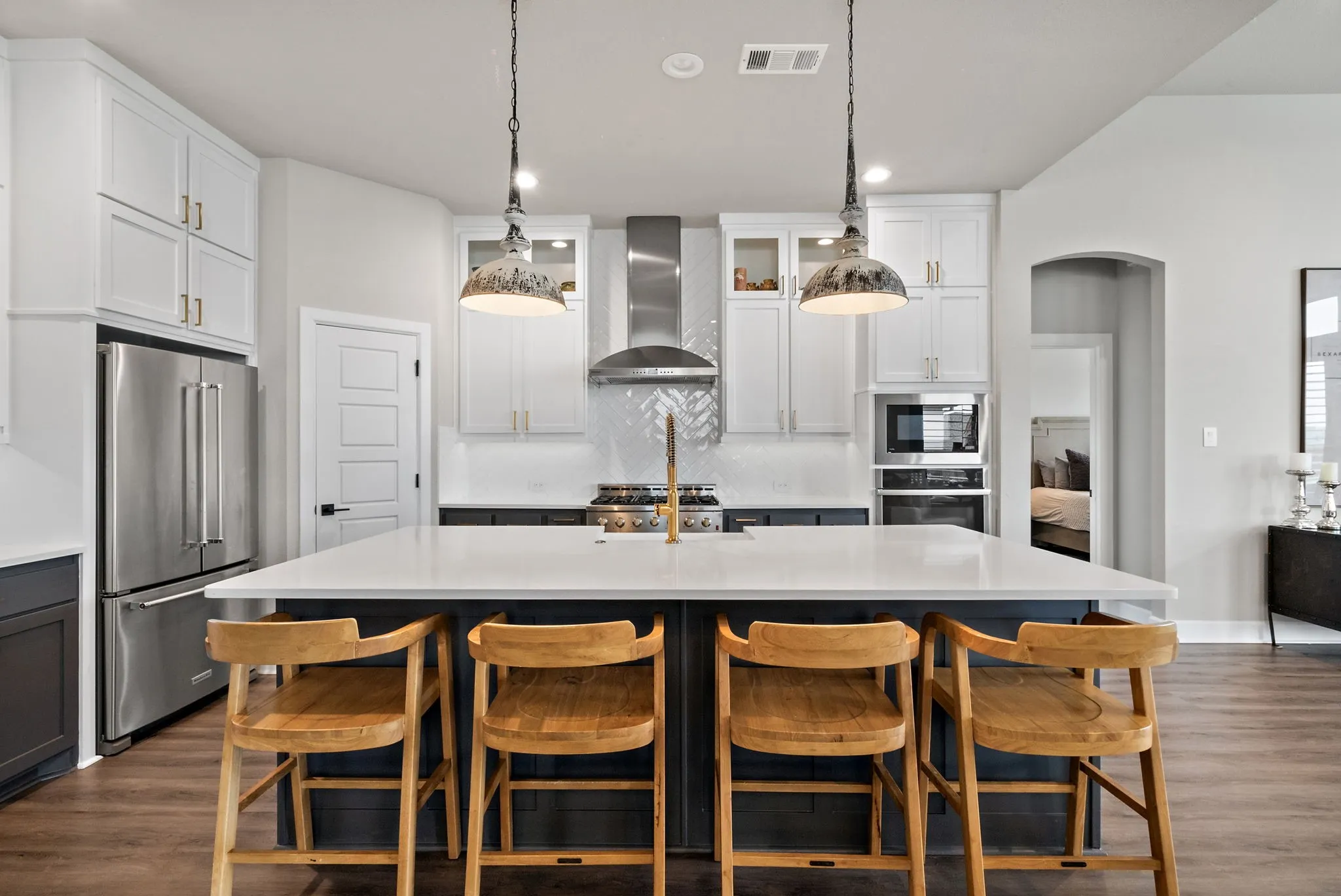 Expansive kitchen island with seating, stainless steel appliances, white perimeter cabinetry, dark wood-finish flooring, and pendant lighting
