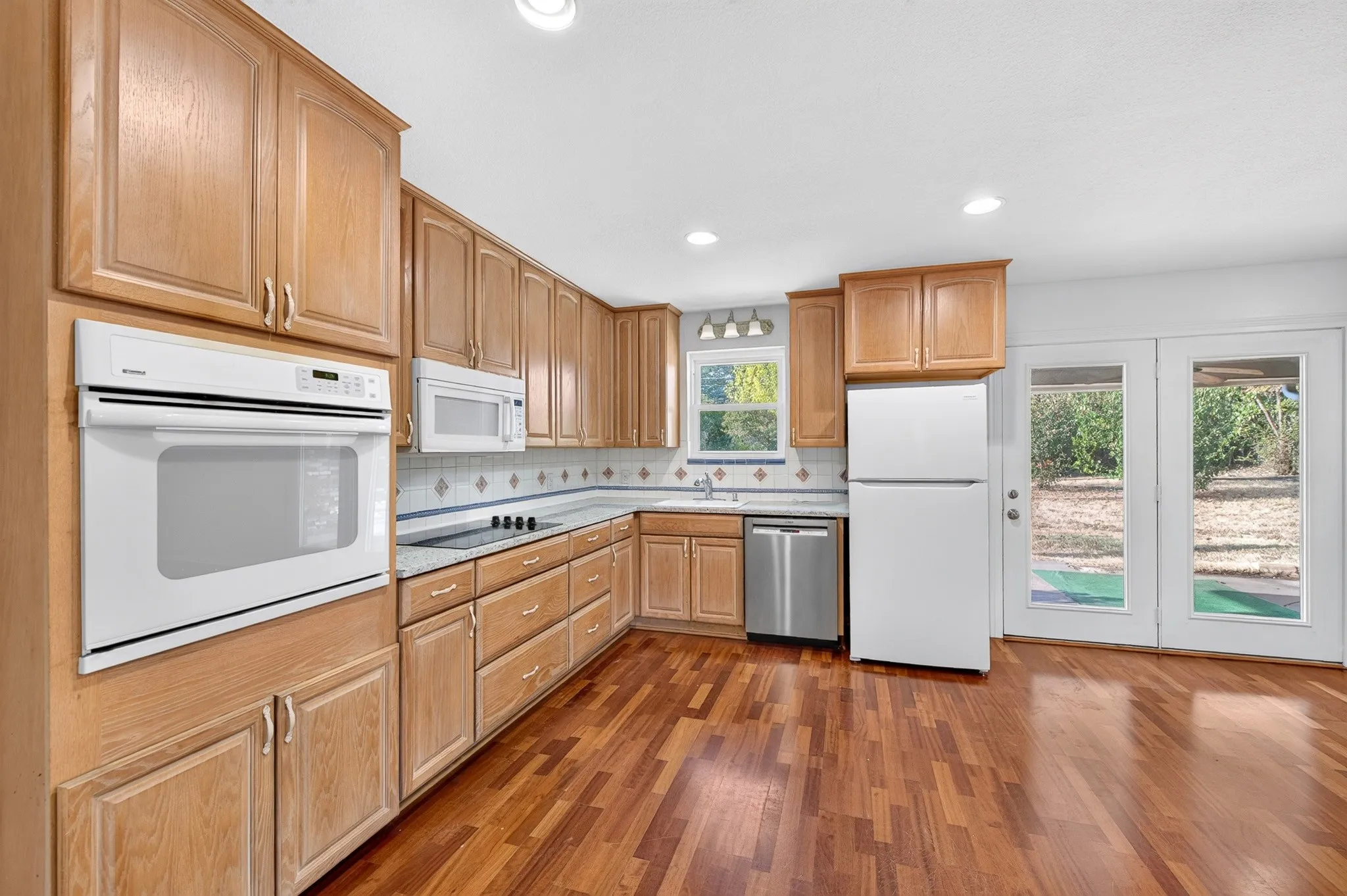 Kitchen featuring wood-finish flooring, light wood cabinetry, white built-in oven, and double French doors with exterior access