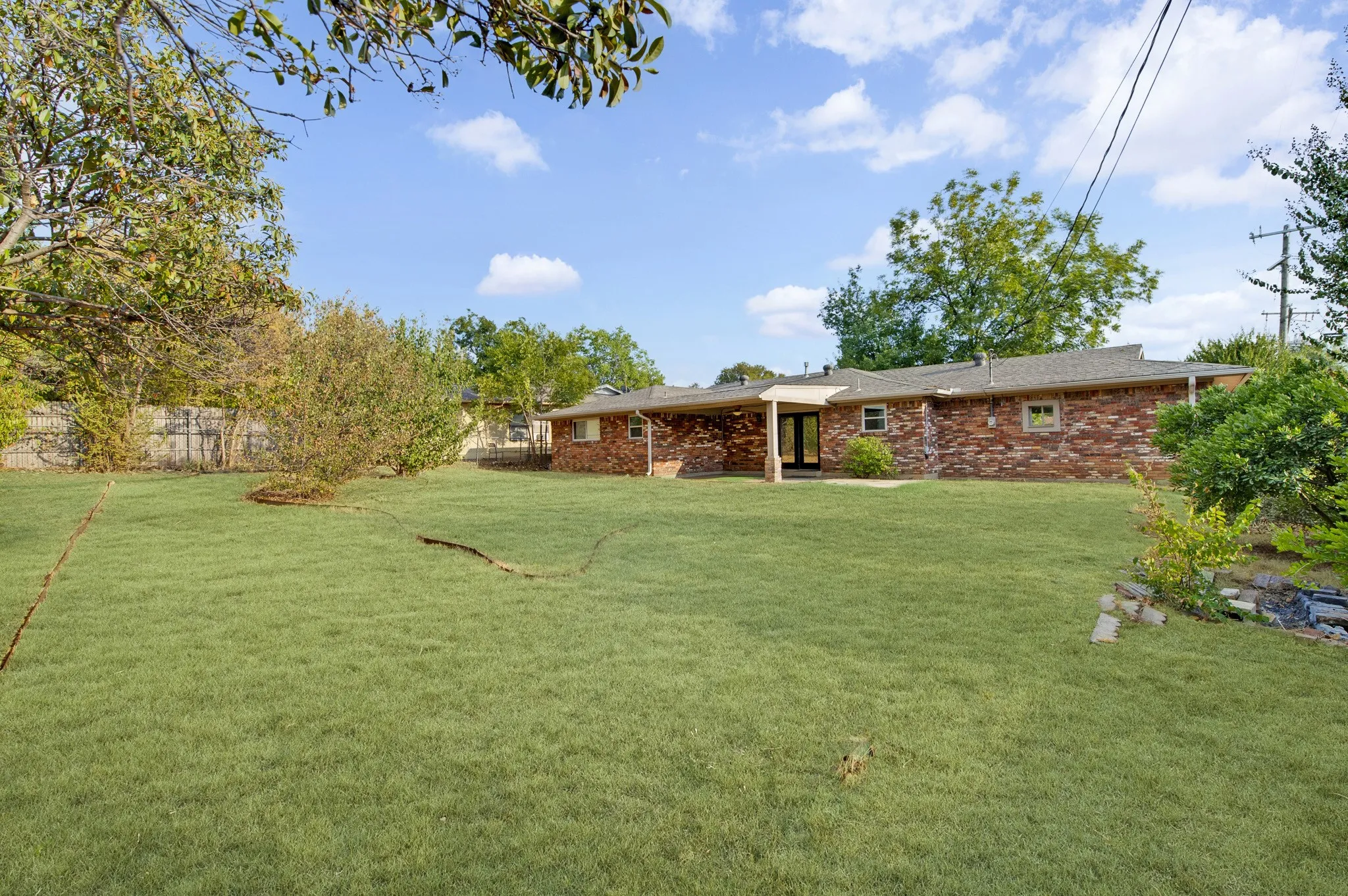Expansive lawn featuring mature trees, a brick-clad exterior, and an exterior covered patio
