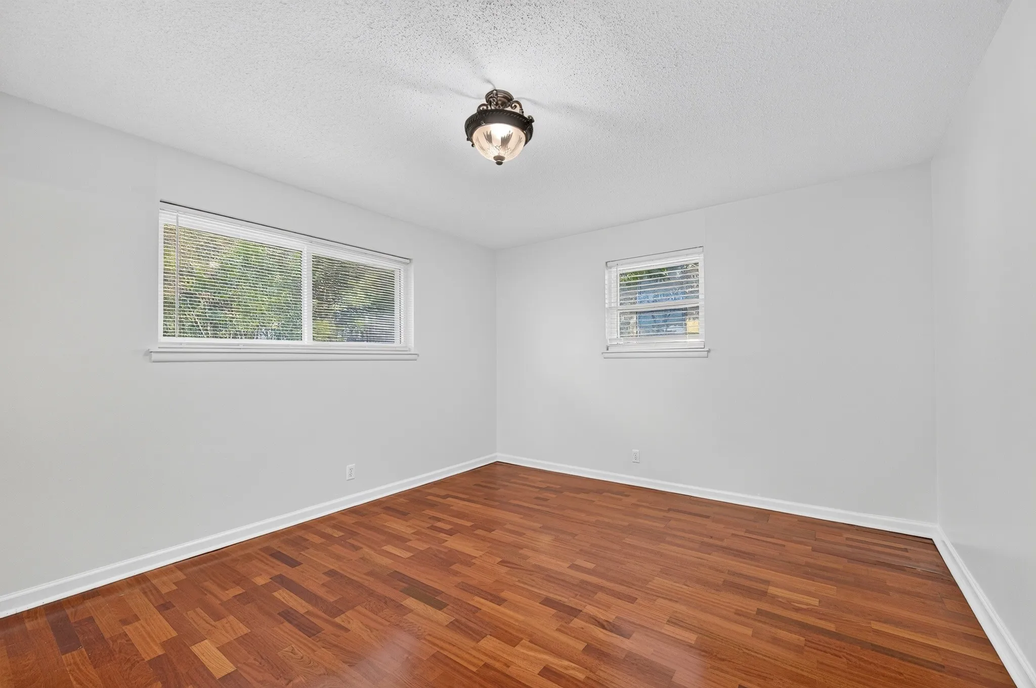 Wood-finish flooring with white baseboards, white walls, and a textured ceiling