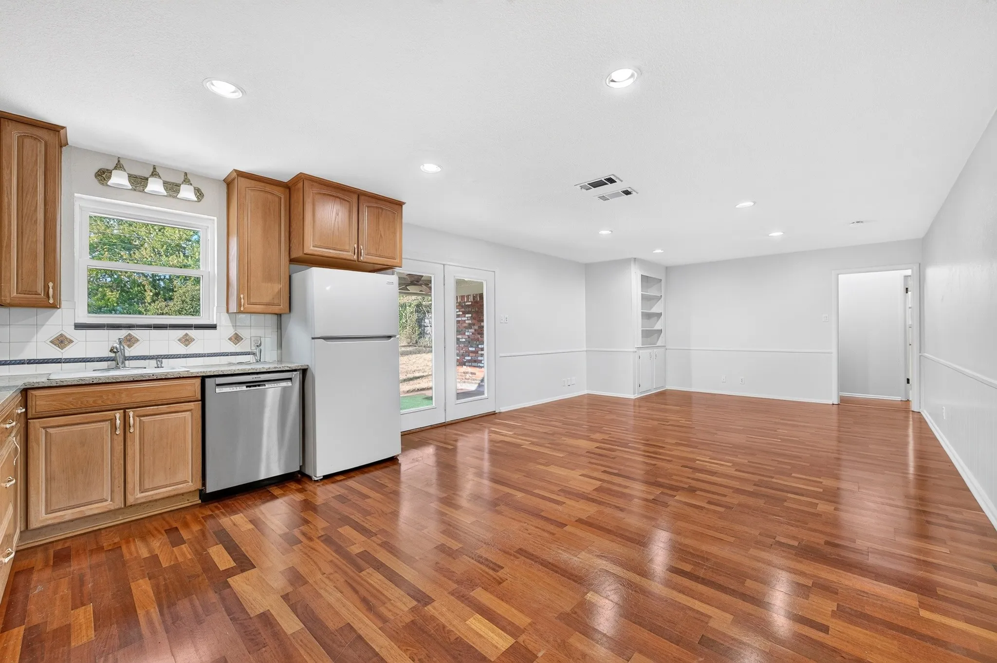 Wood-finish flooring, recessed lighting, built-in shelving, white cabinetry, and stainless steel dishwasher