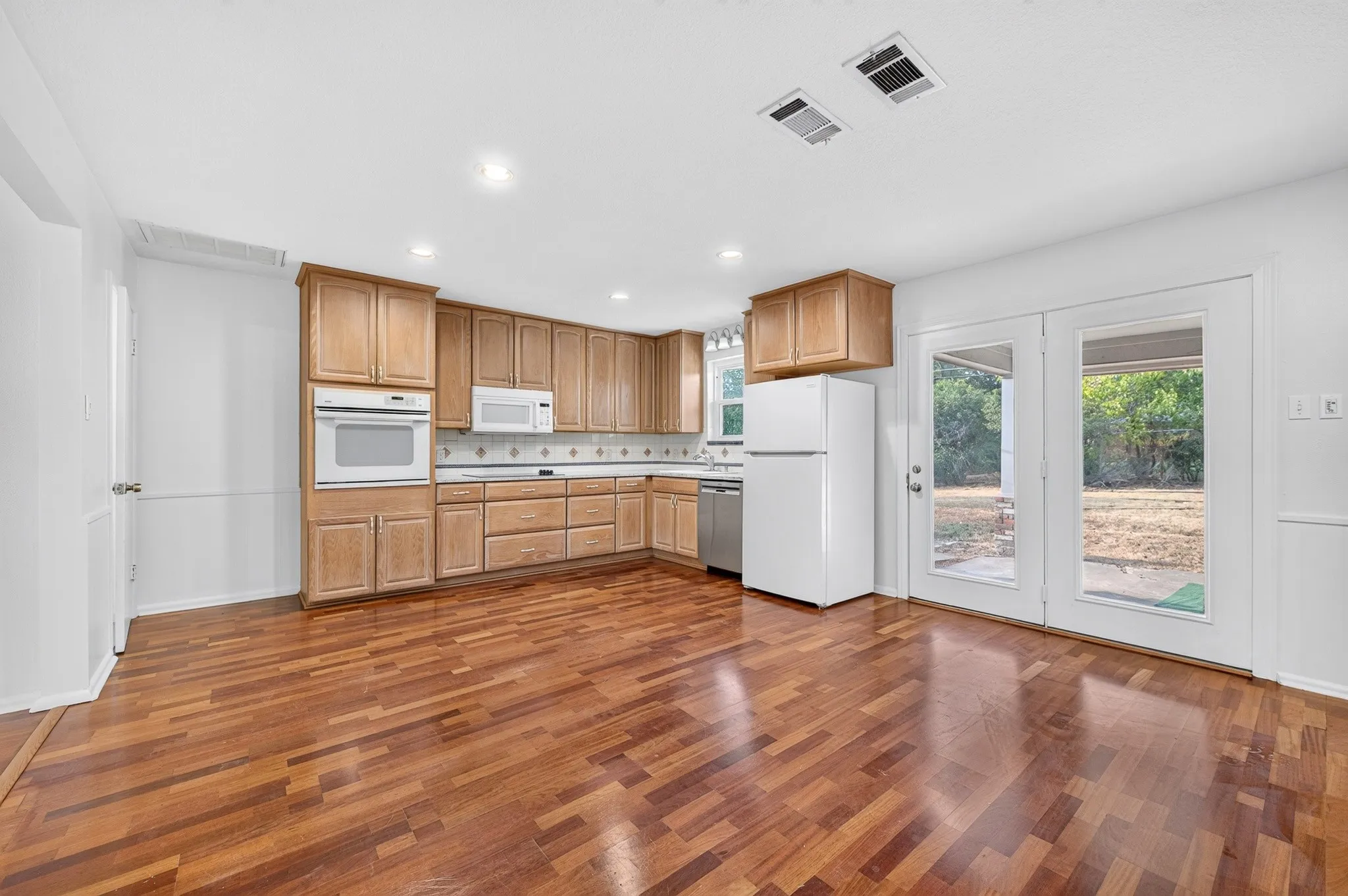 Kitchen featuring wood-finish flooring, light wood cabinetry, white appliances, and a tiled backsplash