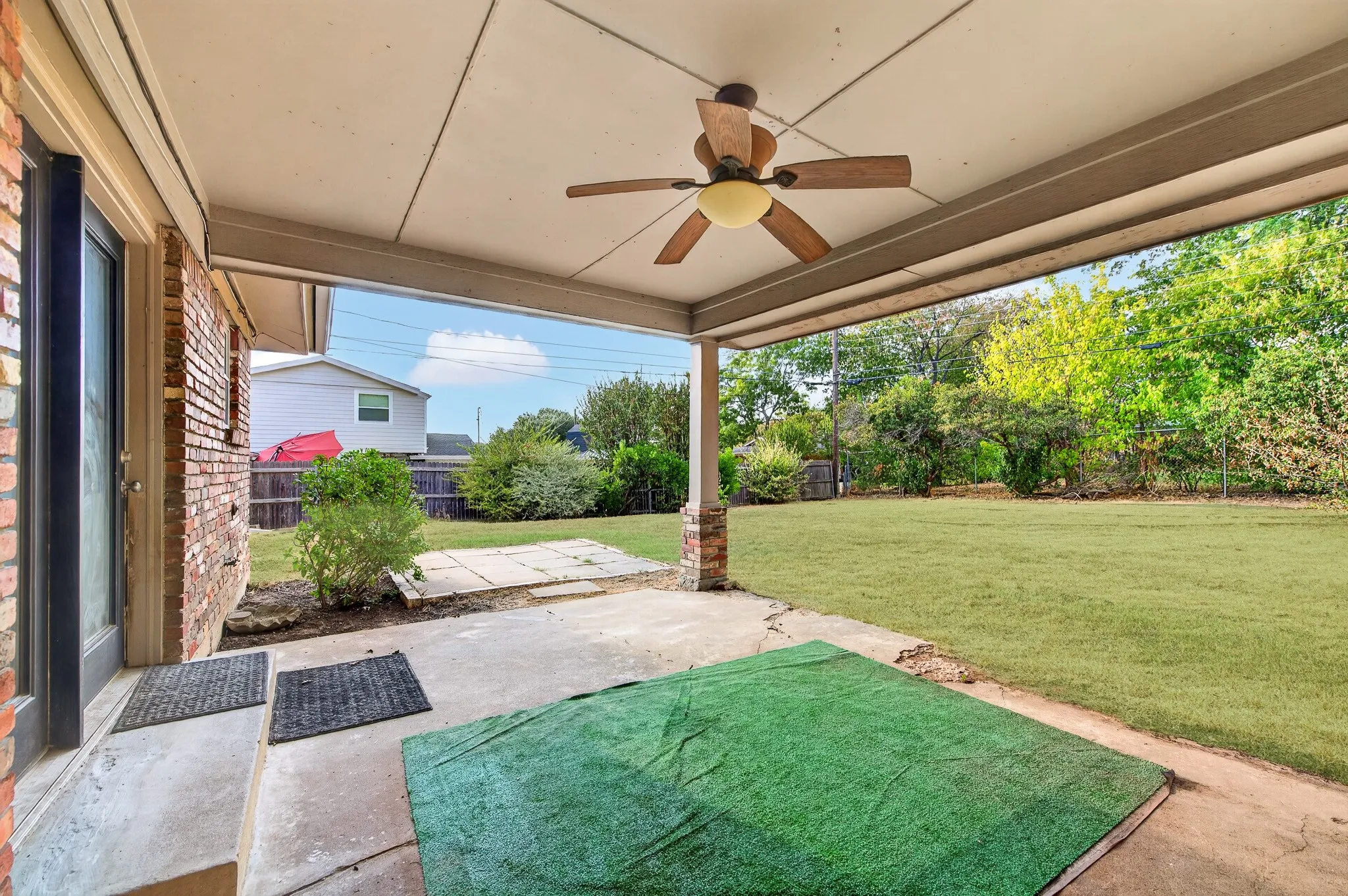 Covered patio featuring a ceiling fan, brick accent columns, and a concrete surface