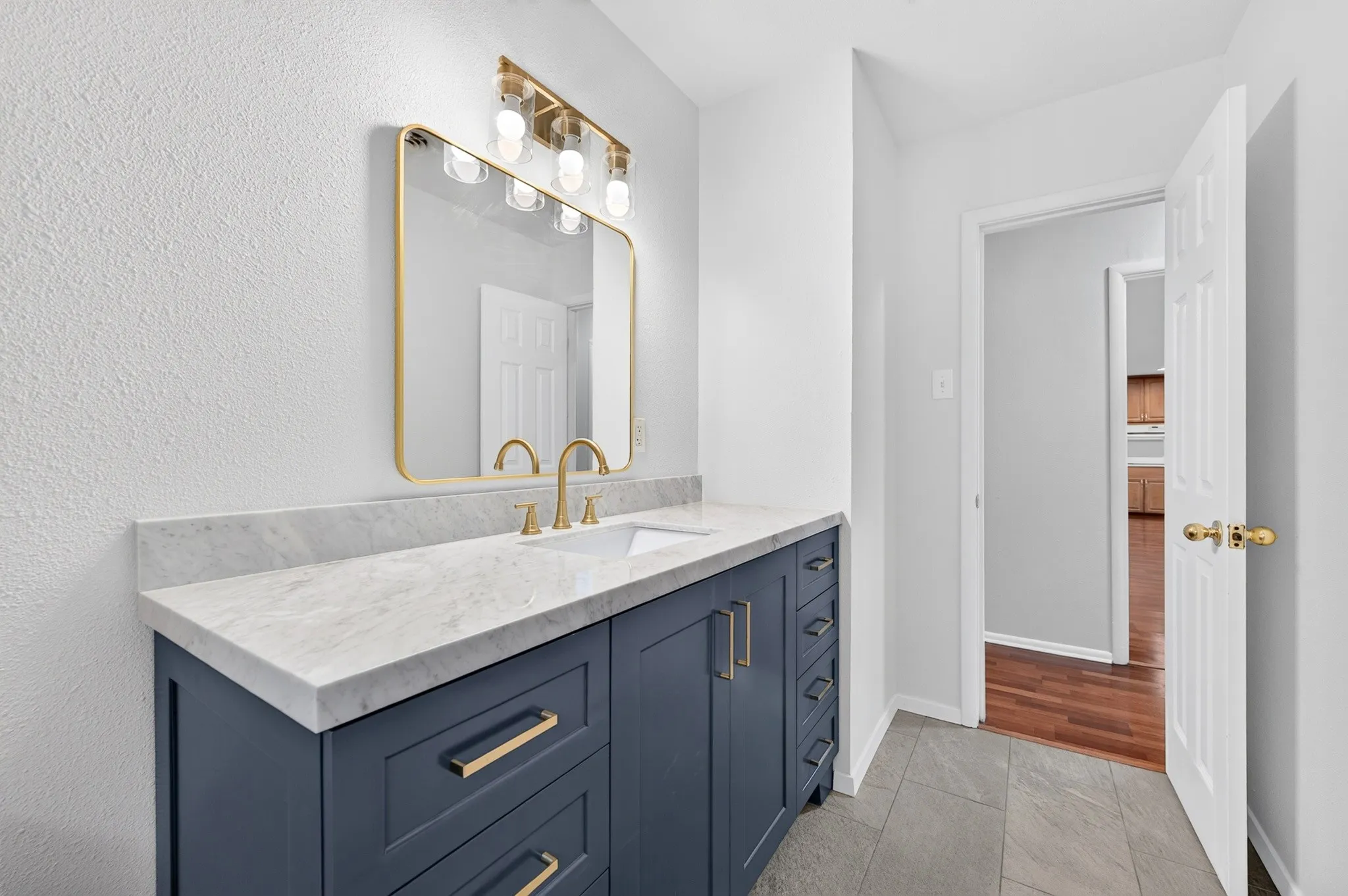 Bathroom vanity featuring a light-toned countertop, integrated rectangular sink, and a gold-framed mirror with an overhead light fixture