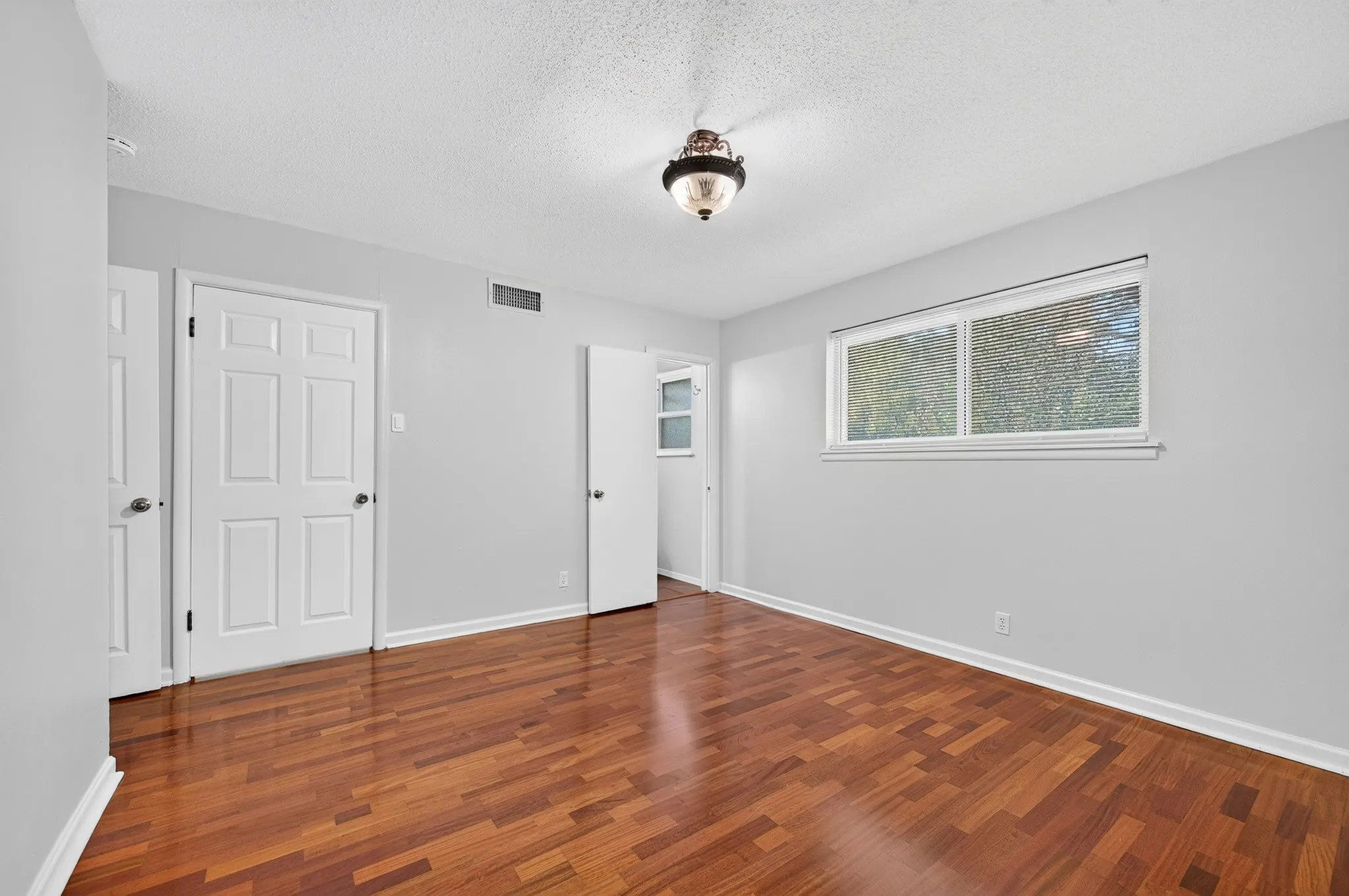 Wood-finish flooring, white paneled doors, and a decorative semi-flush mount light fixture