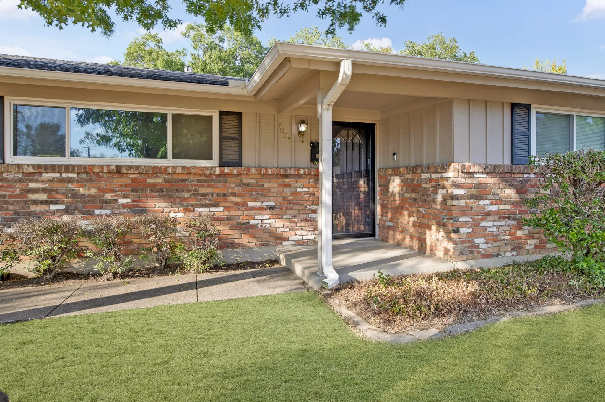 Brick exterior with a covered entry, decorative security screen door, and multiple windows