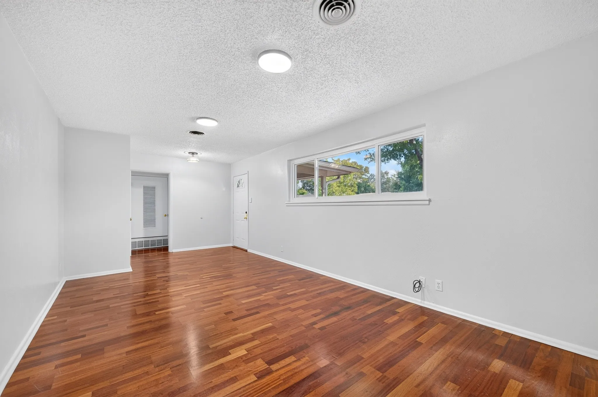 Wood-finish flooring, white walls, multiple flush-mount ceiling lights, and an exterior door with frosted glass