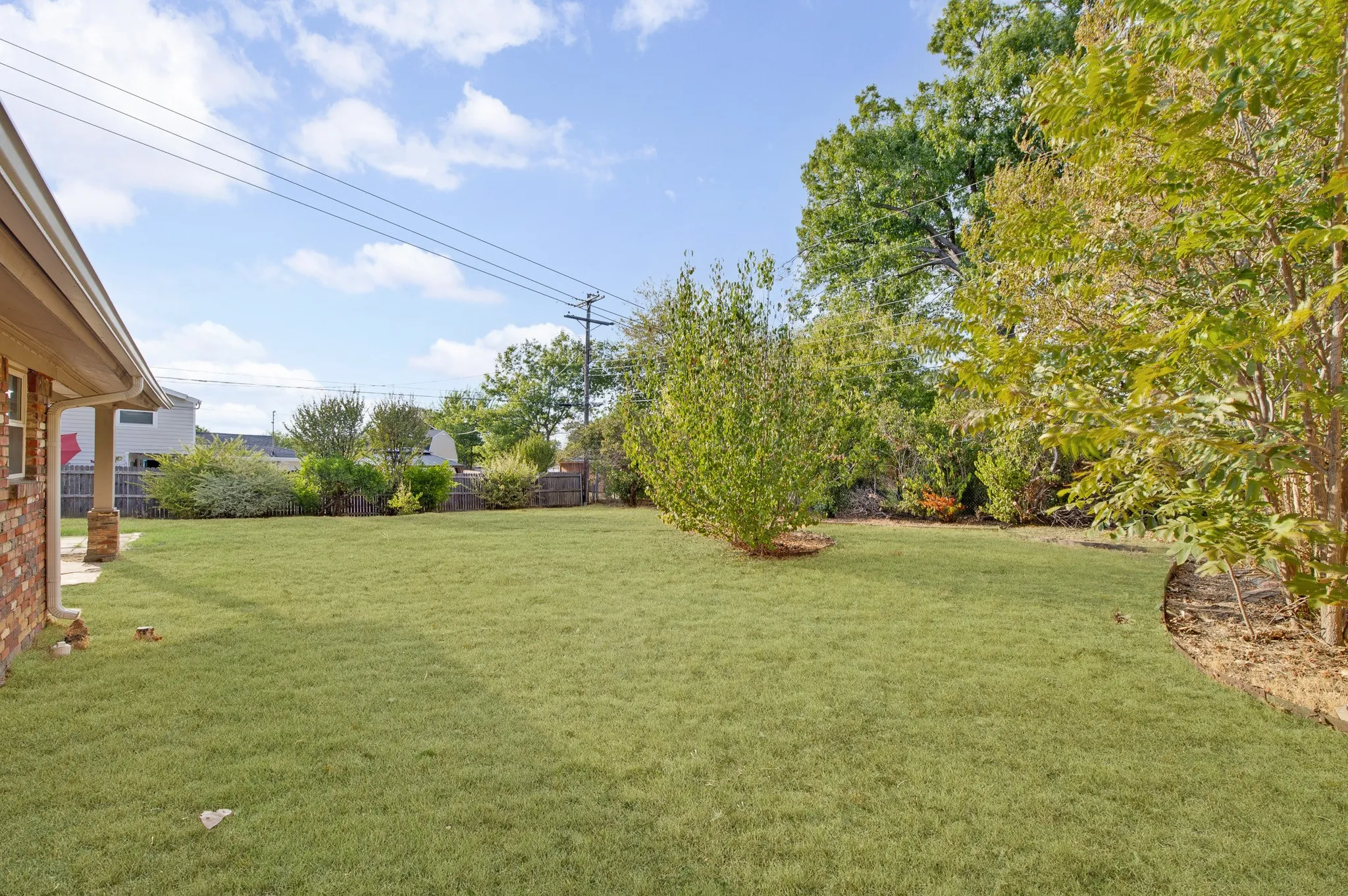 Expansive backyard featuring a manicured lawn, mature trees, and a covered patio with brick columns