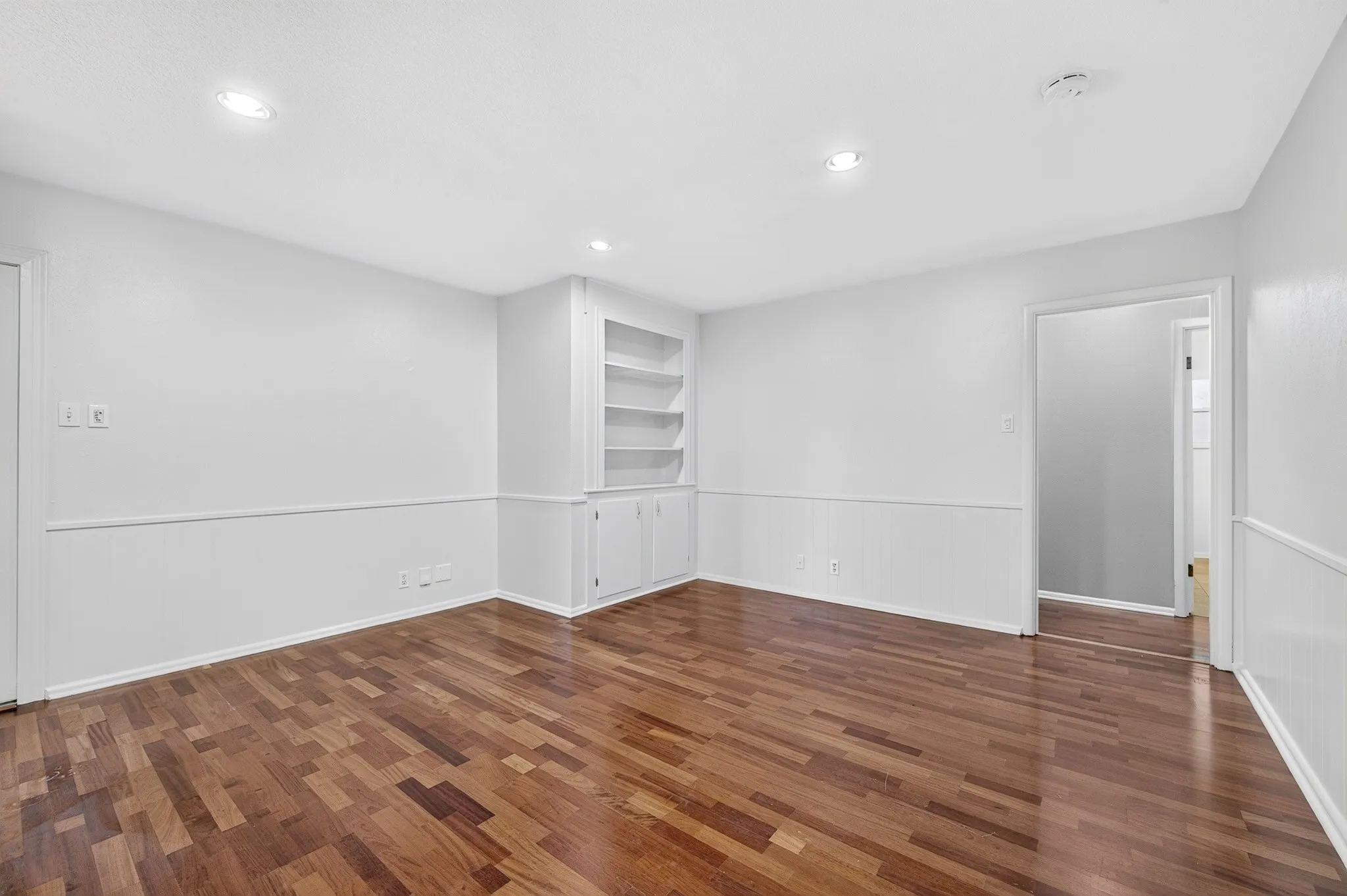 Wood-finish flooring with recessed lighting, built-in shelving, and wainscoting