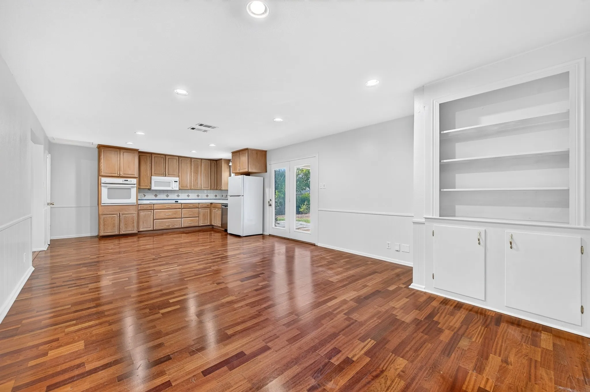 Hardwood flooring throughout, kitchen with wood cabinetry, built-in wall oven, built-in microwave, and French doors