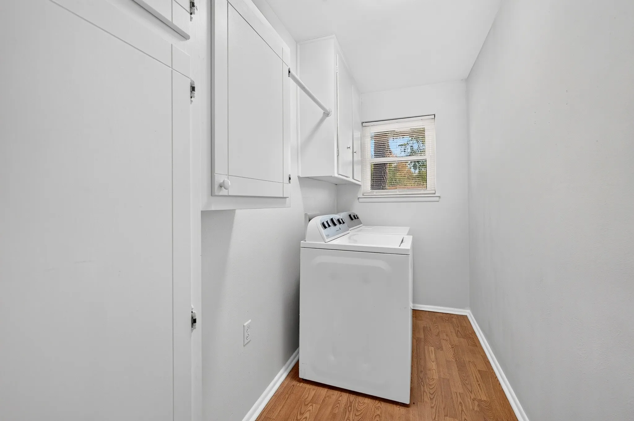 Wood-finish flooring with white baseboards, a single window, and a built-in wall cabinet