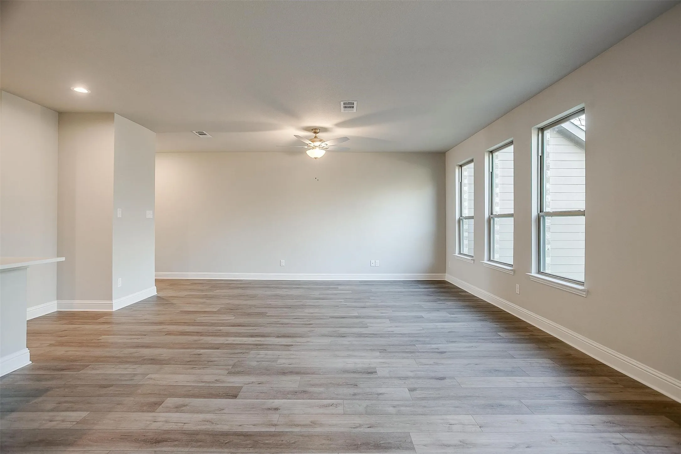 Spacious room featuring wood-finish flooring, multiple windows, a ceiling fan, and recessed lighting