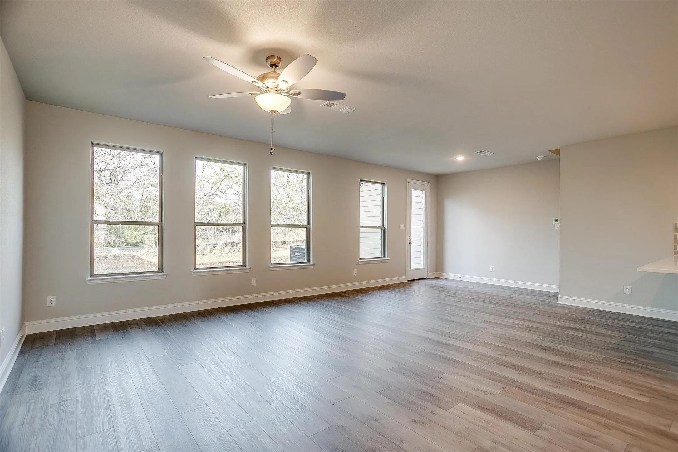 Spacious room featuring wood-finish flooring, multiple windows, a ceiling fan with integrated lighting, recessed lighting, and a glass-paneled door