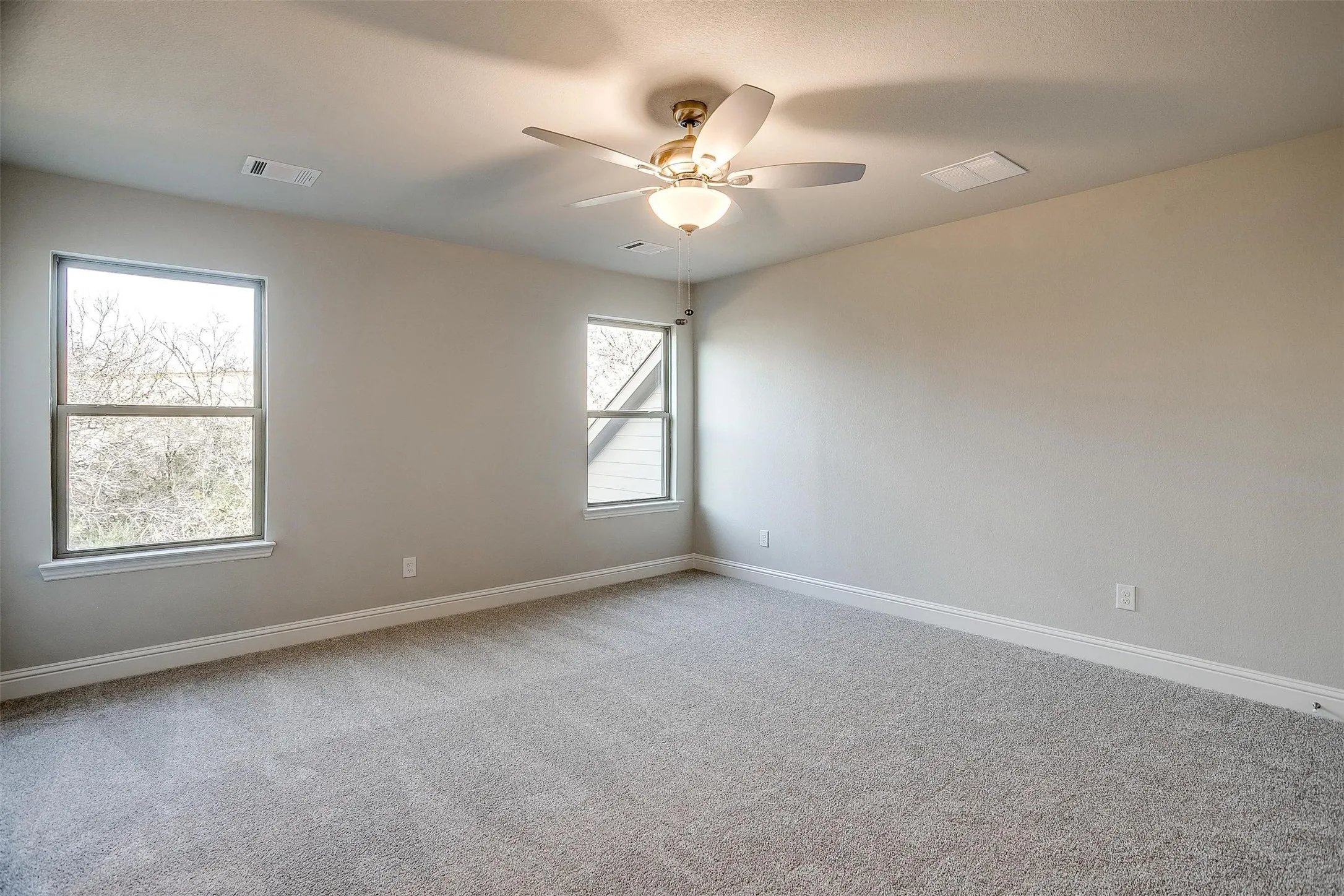 Plush carpeting, neutral wall tones, two windows with white trim, and a ceiling fan with integrated lighting