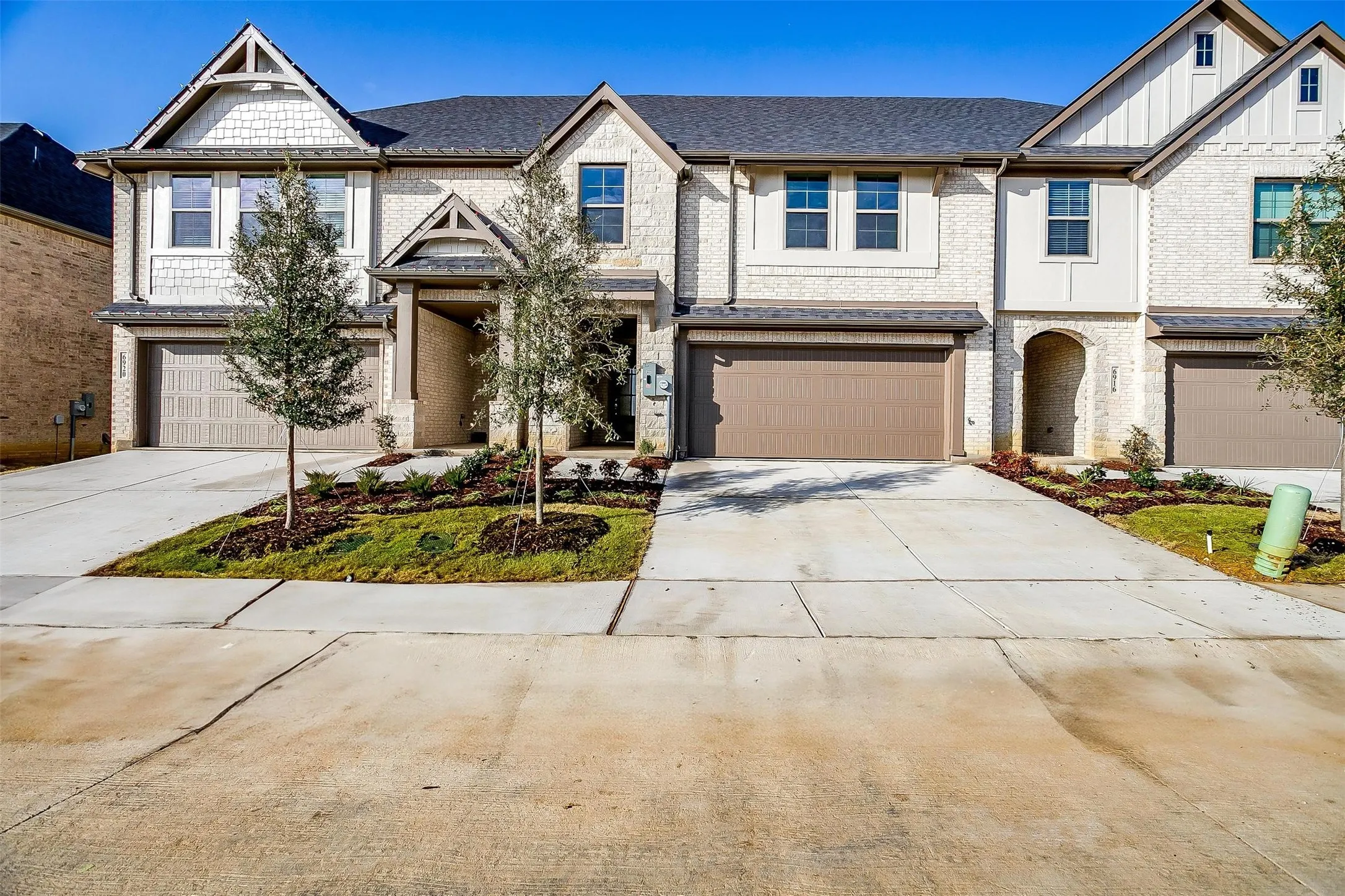Stone and siding exterior with dark trim accents, multiple garage doors, and landscaped front yards