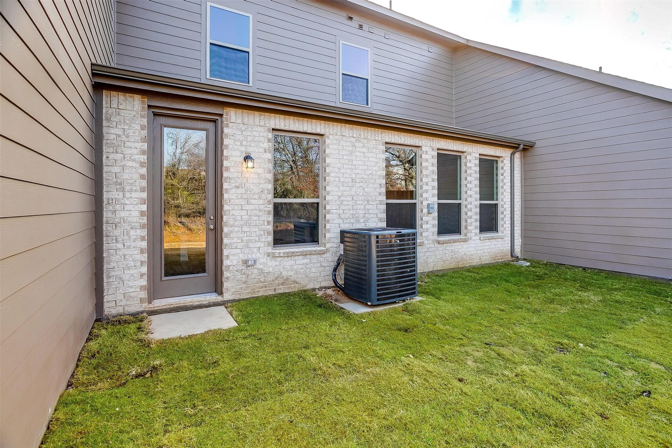 Exterior featuring a full-light door, multiple windows, a modern outdoor light fixture, and a compact grass area