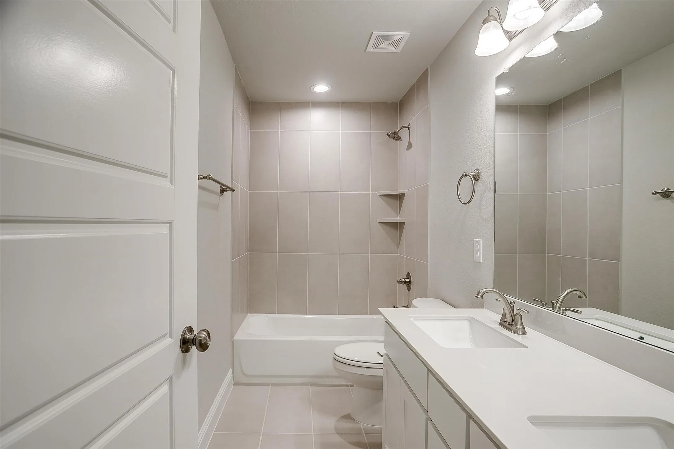 Bathroom featuring a built-in tub with tile surround, a vanity with dual sinks, and a large mirror