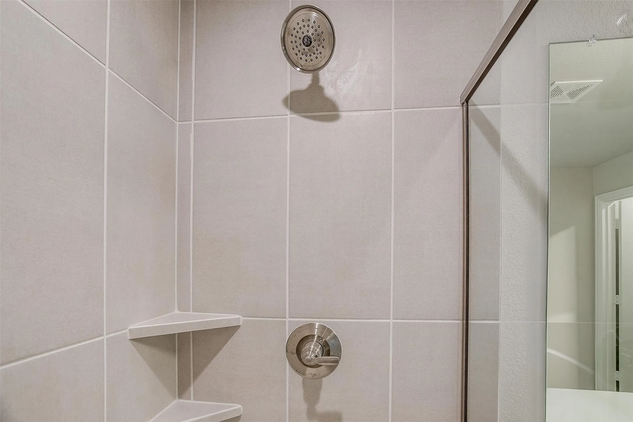 Tiled shower with a rainfall showerhead, brushed nickel fixtures, and built-in corner shelving