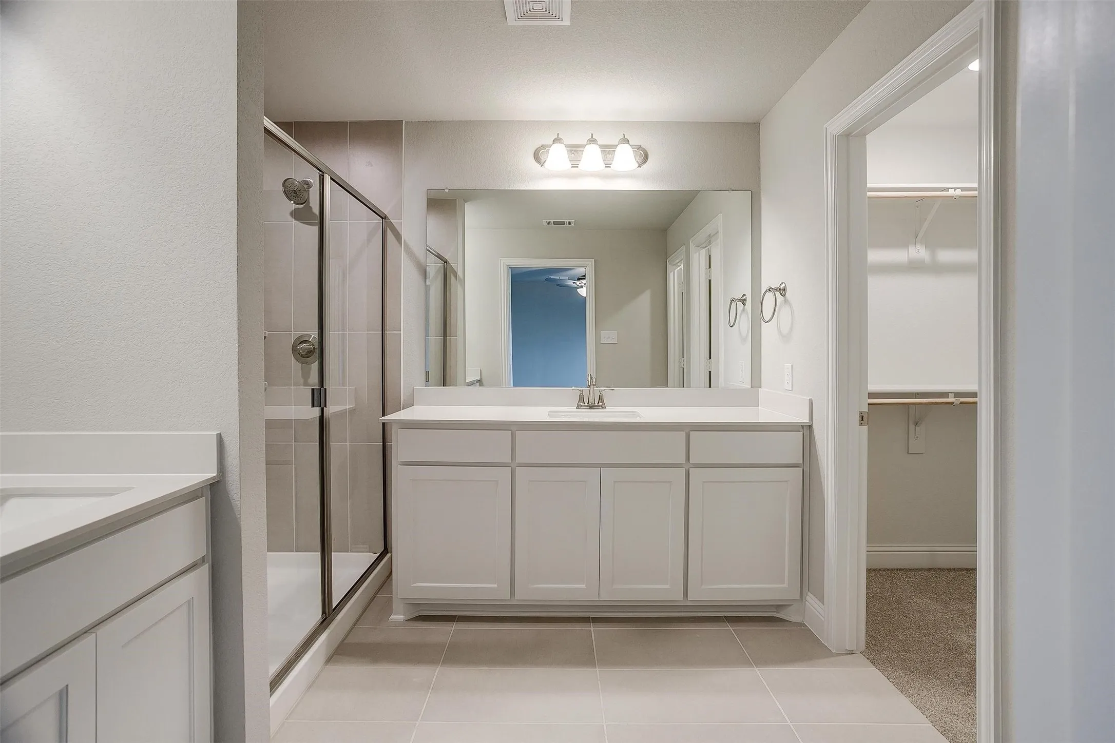 White vanity with a light-colored countertop, framed mirror, and a glass-enclosed shower with tile surround
