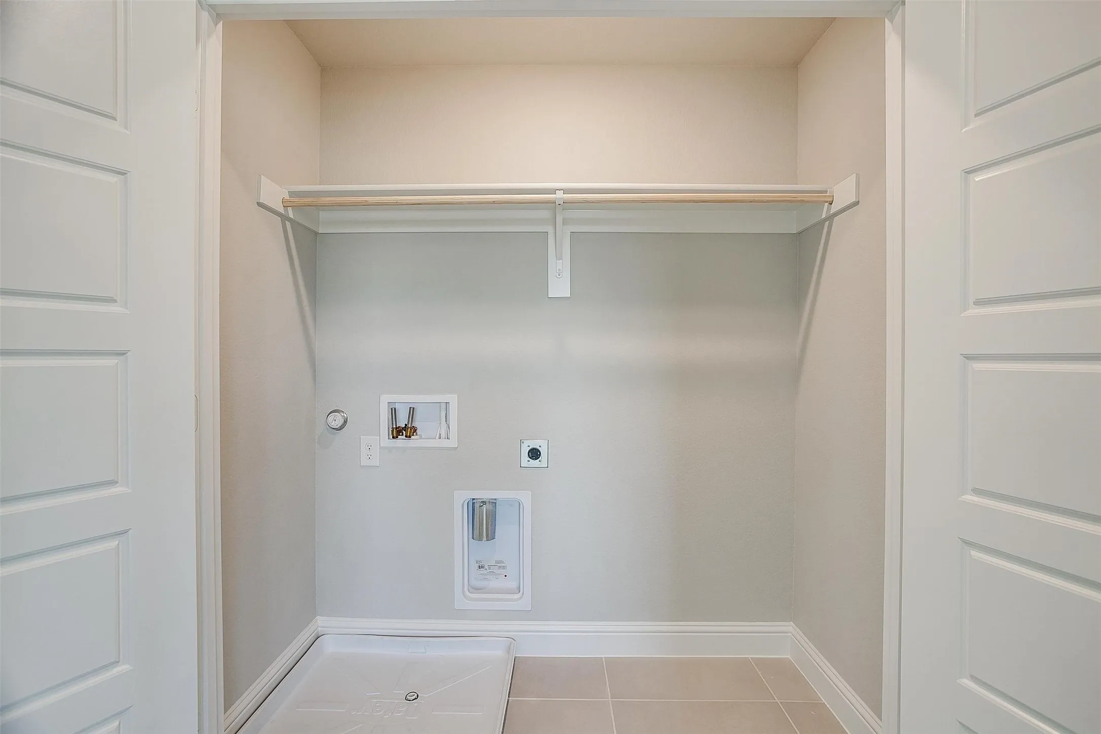 Laundry area with tile flooring, a hanging rod, and paneled doors