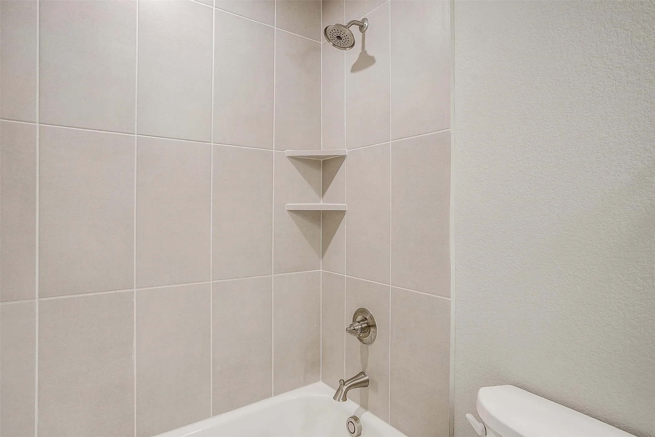 Tiled shower with integrated corner shelving, brushed nickel fixtures, and a white bathtub