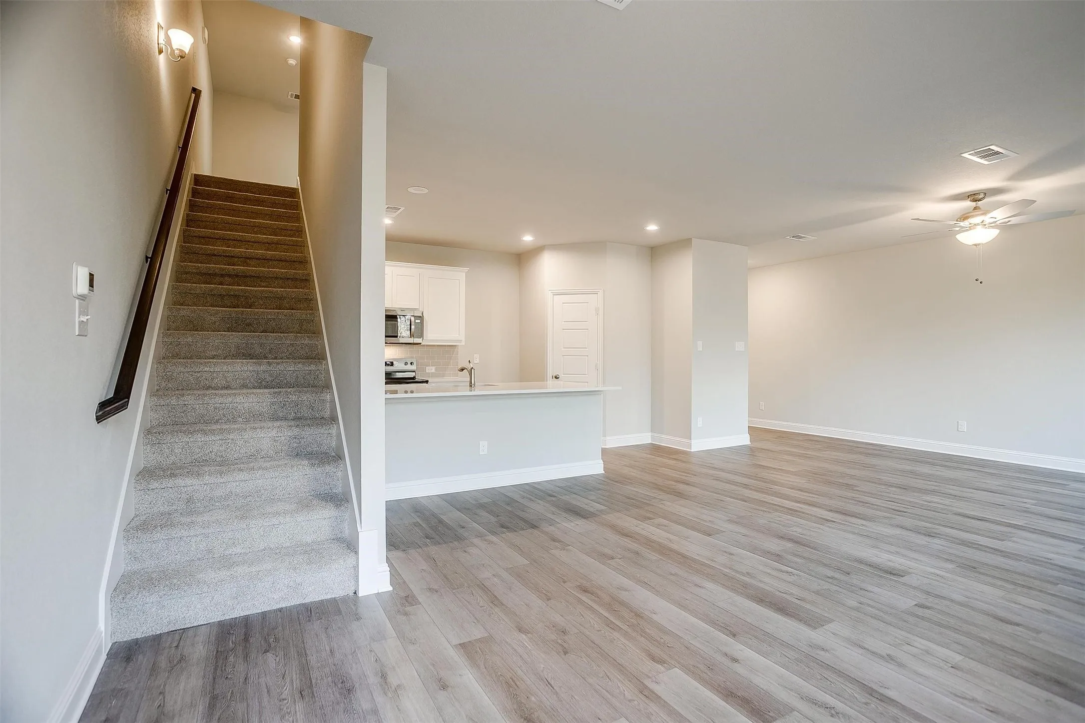 Open-concept living space featuring wood-finish flooring, a contemporary ceiling fan, and a kitchen with white cabinetry and stainless steel appliances