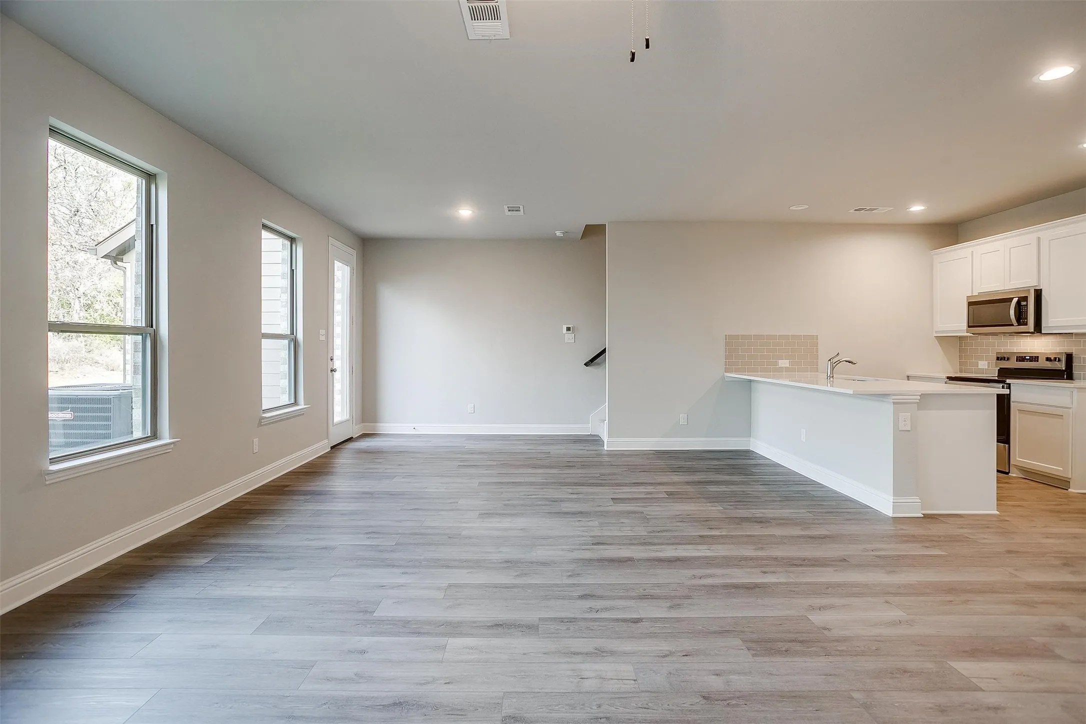 Wood-finish flooring, recessed lighting, white cabinetry, stainless steel appliances, and a tile backsplash
