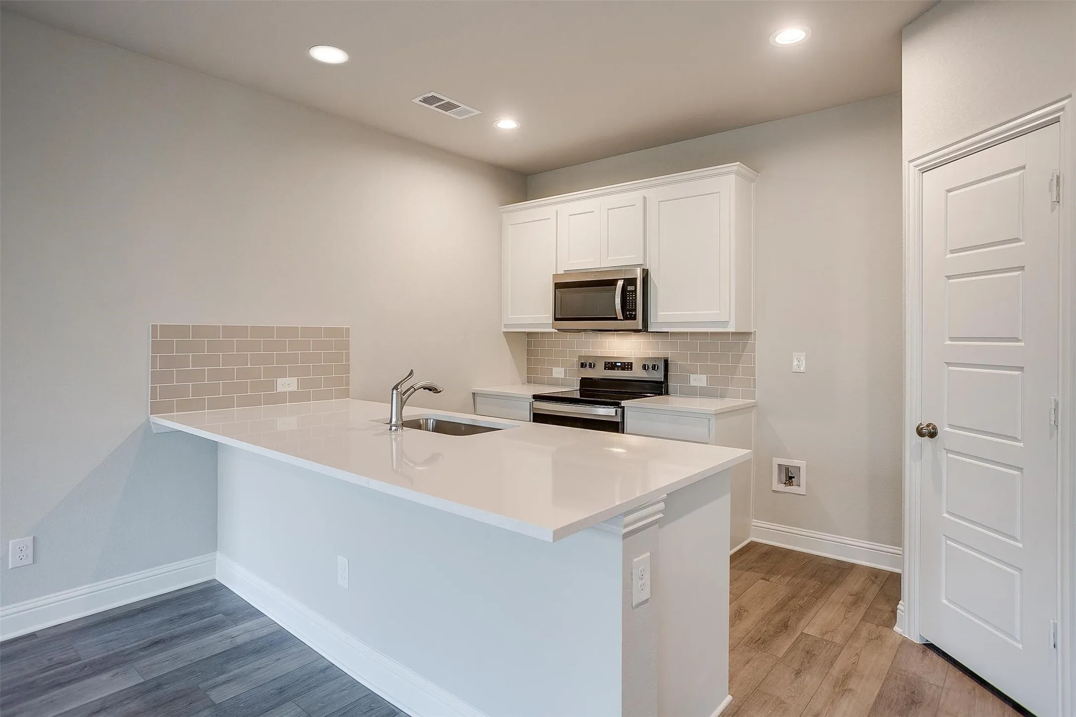 Kitchen with white cabinetry, stainless steel appliances, a white countertop island with a sink, and wood-finish flooring