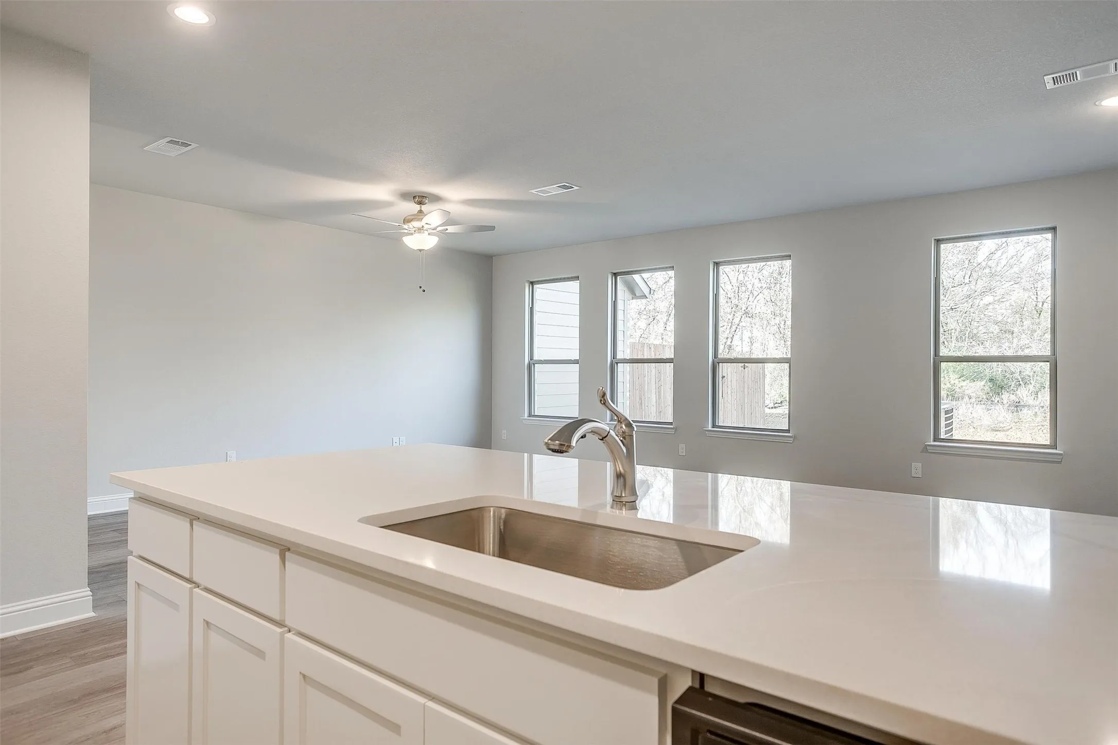 Kitchen island with an undermount sink, gooseneck faucet, light-toned countertop, and white cabinetry