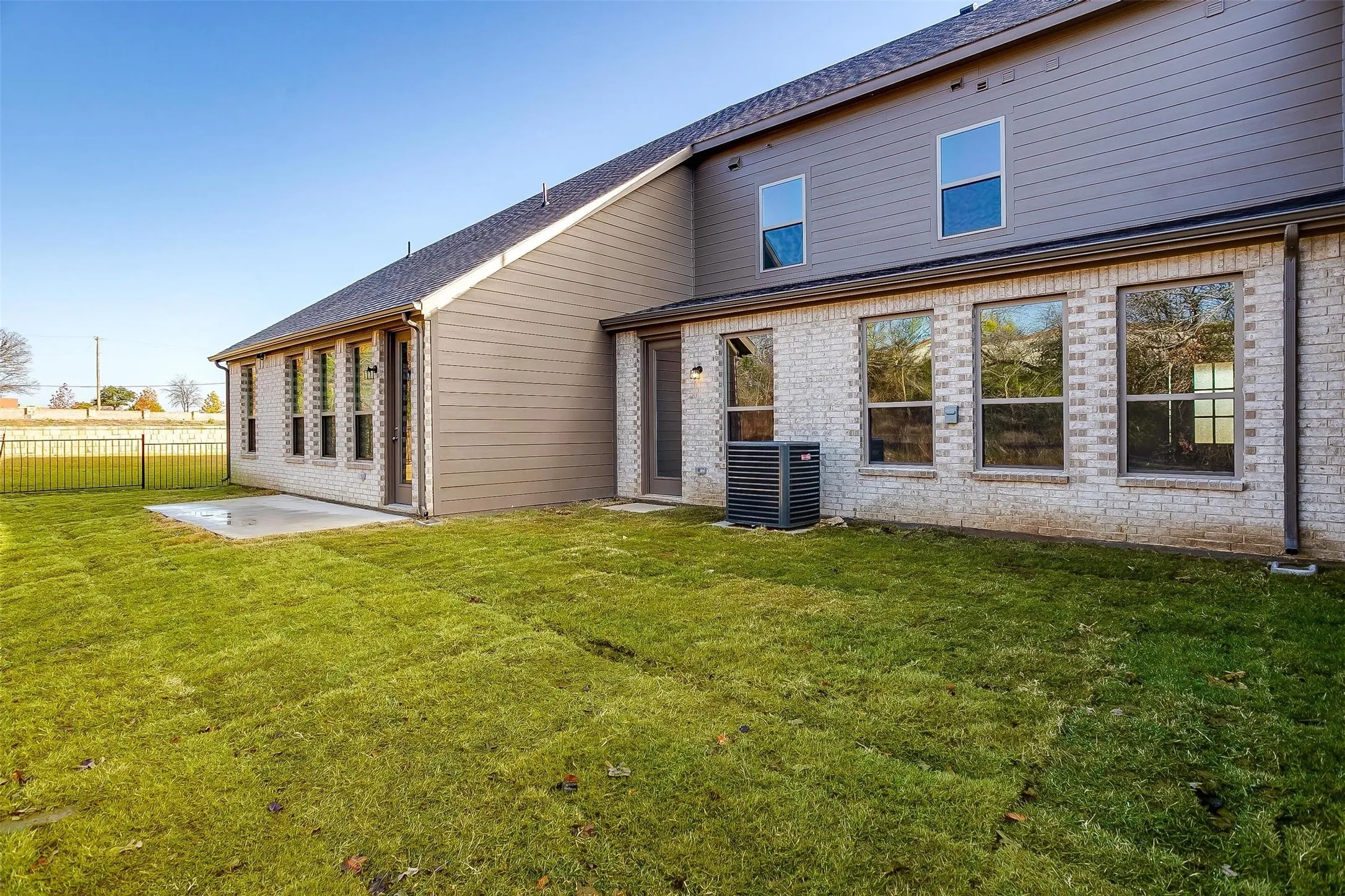 Expansive grassy yard with a concrete patio, a full brick lower level, and a multi-pane upper window
