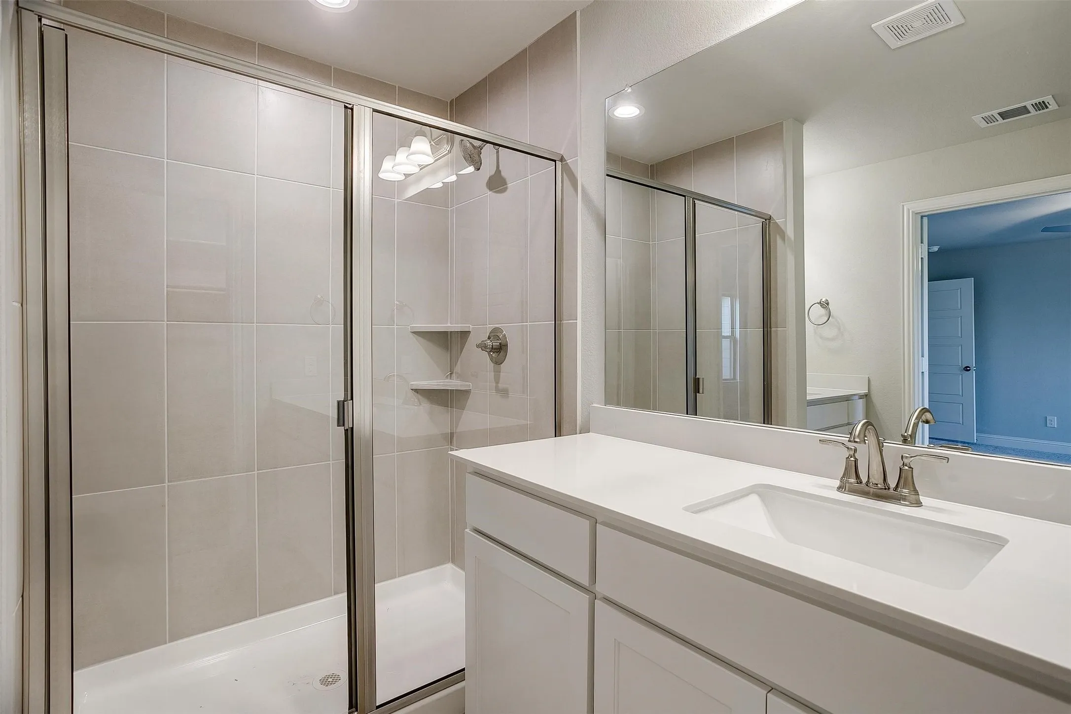 Bathroom featuring a glass-enclosed shower with tile surround, a single vanity with an undermount sink, and a large mirror