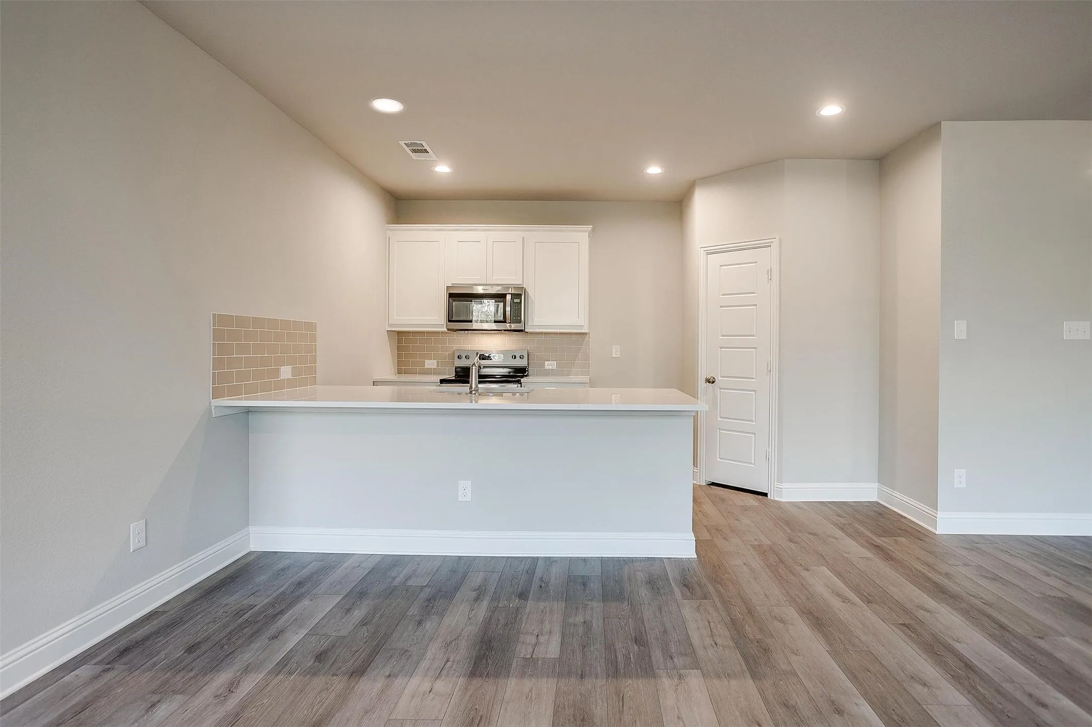 Kitchen featuring a breakfast bar, white cabinetry, stainless steel appliances, tile backsplash, and wood-finish flooring
