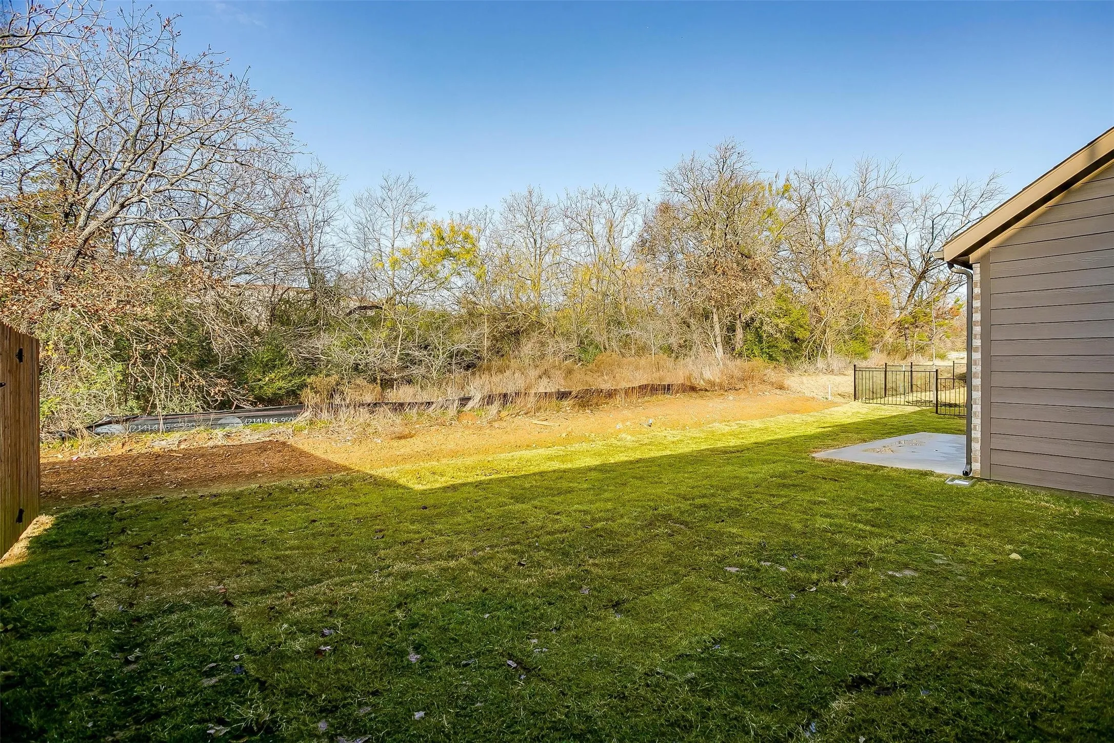 Expansive grassy yard with a concrete patio, wood privacy fence, and a black metal fence