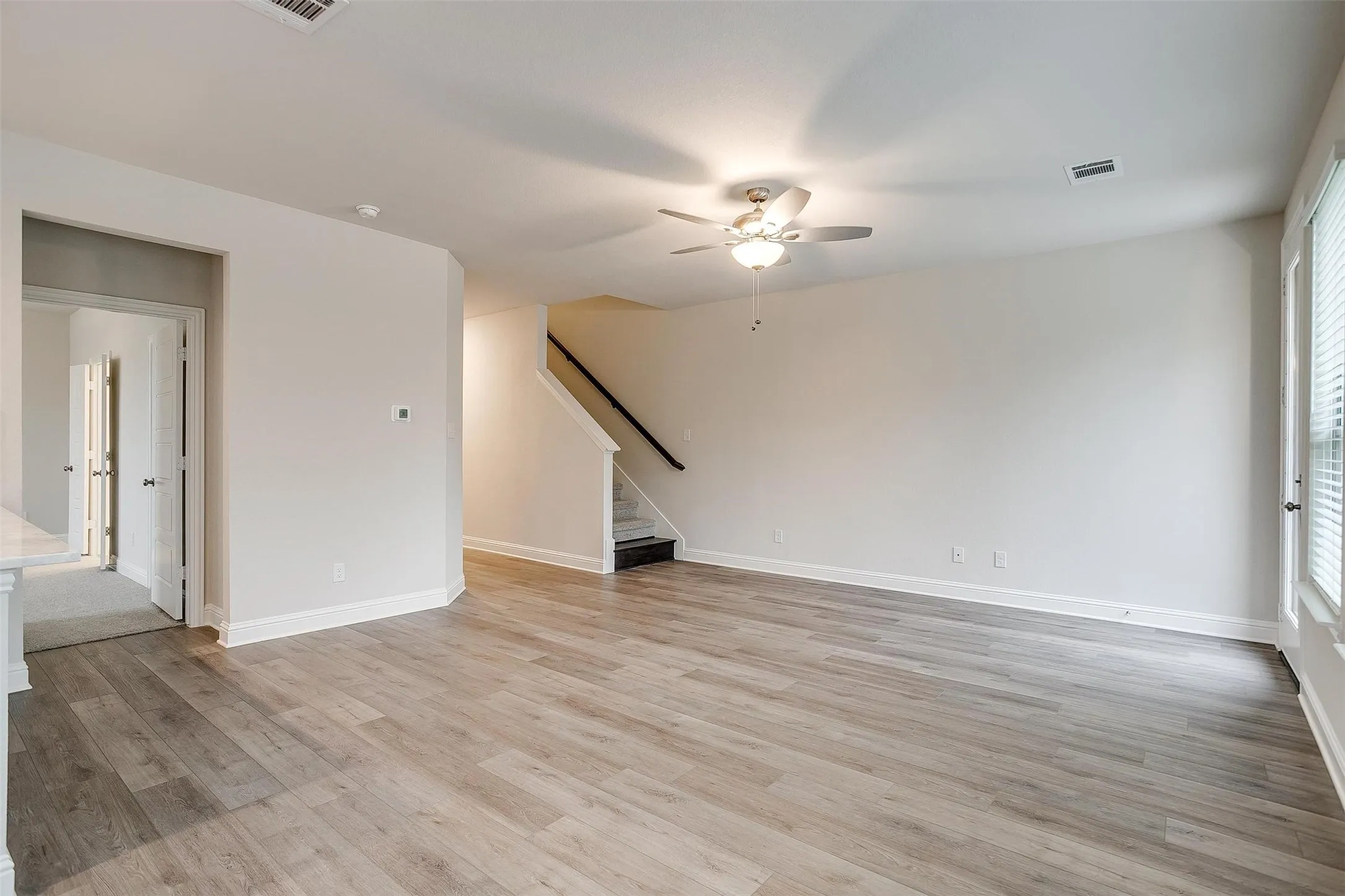 Open-concept living area featuring wood-finish flooring, a ceiling fan with integrated lighting, and white trim throughout