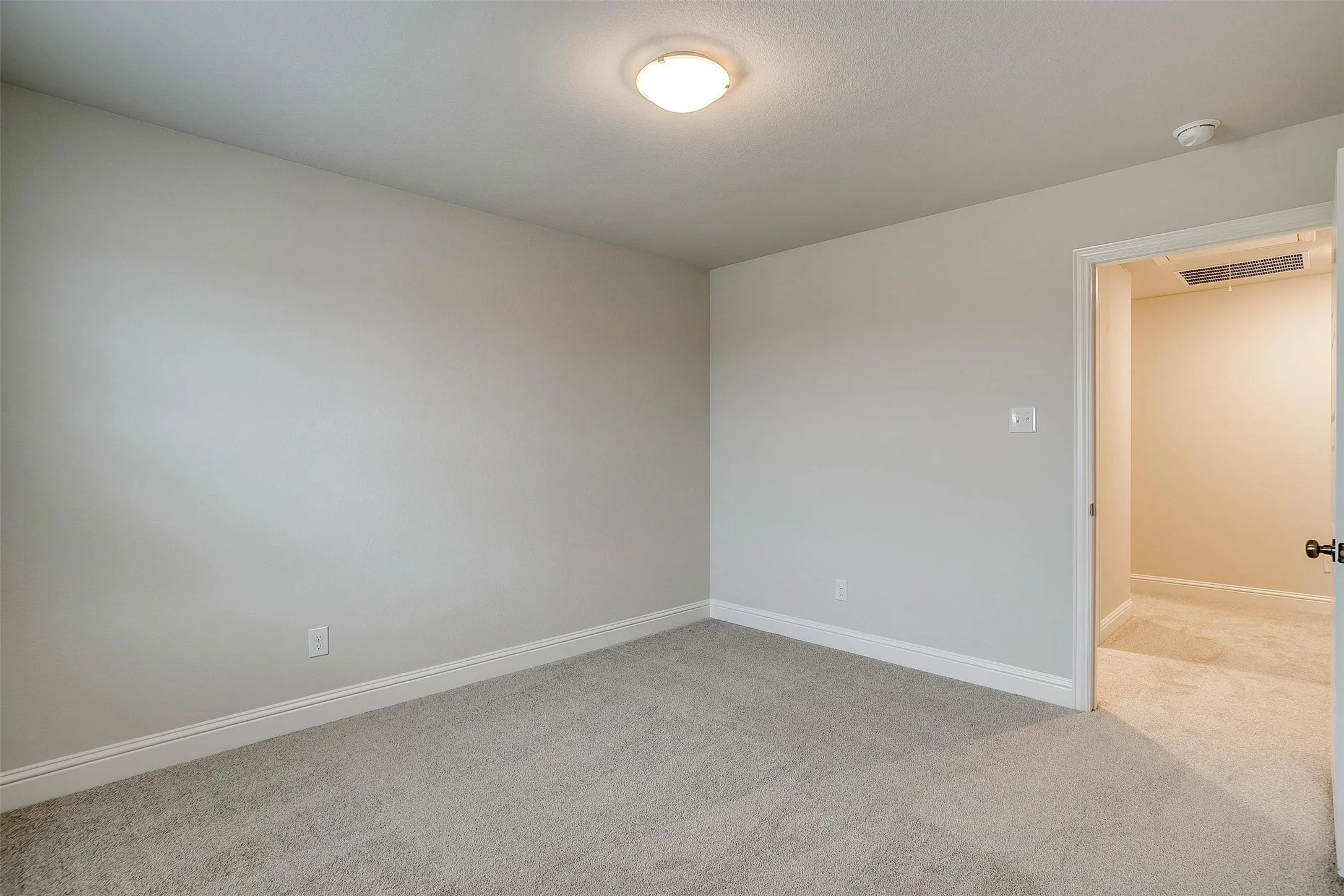 Neutral tone wall paint, light gray carpeting, flush mount ceiling light, white trim