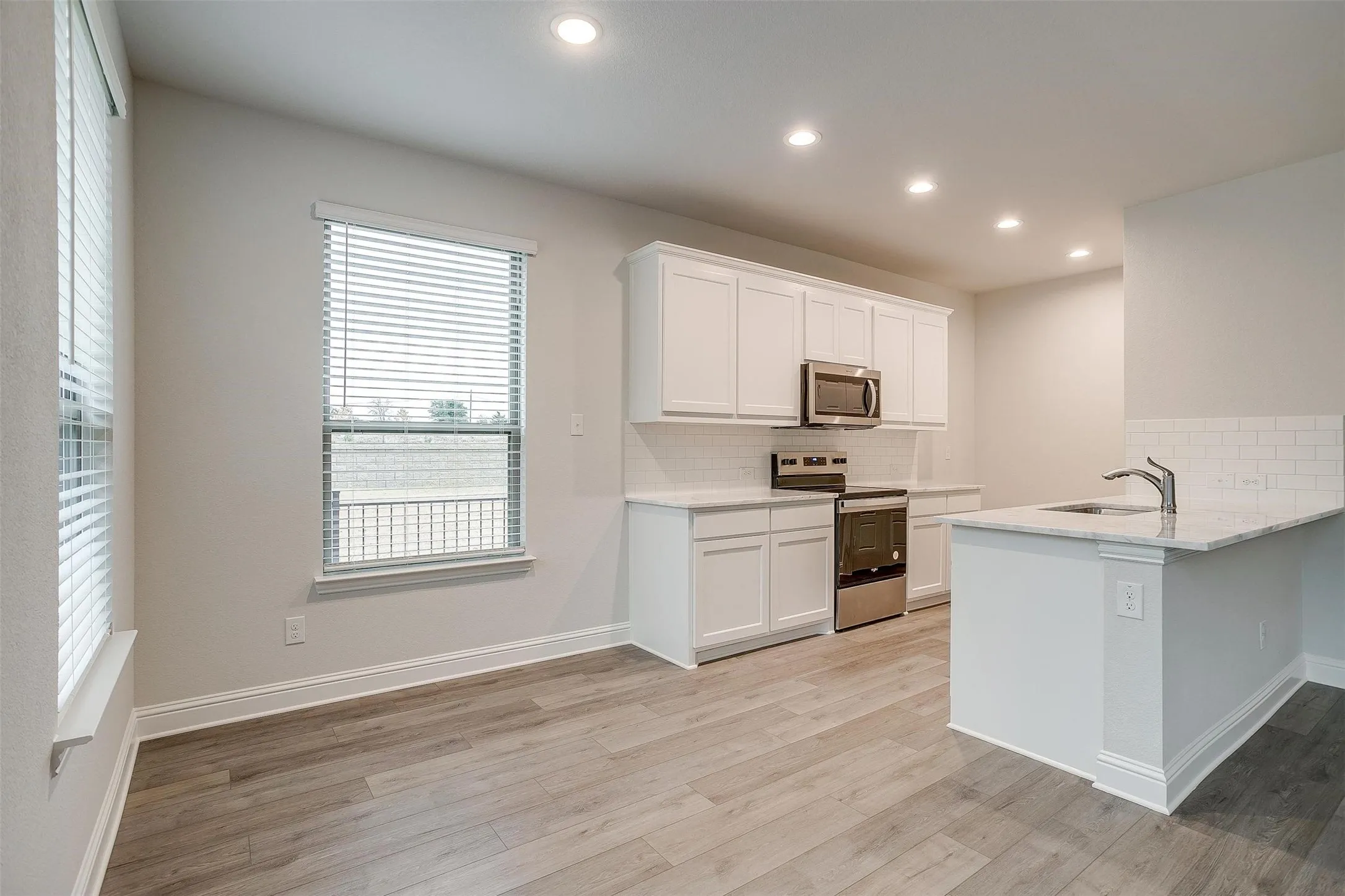 Kitchen and dining area featuring wood-finish flooring, recessed lighting, white cabinetry, stainless steel appliances, and a kitchen island with a sink