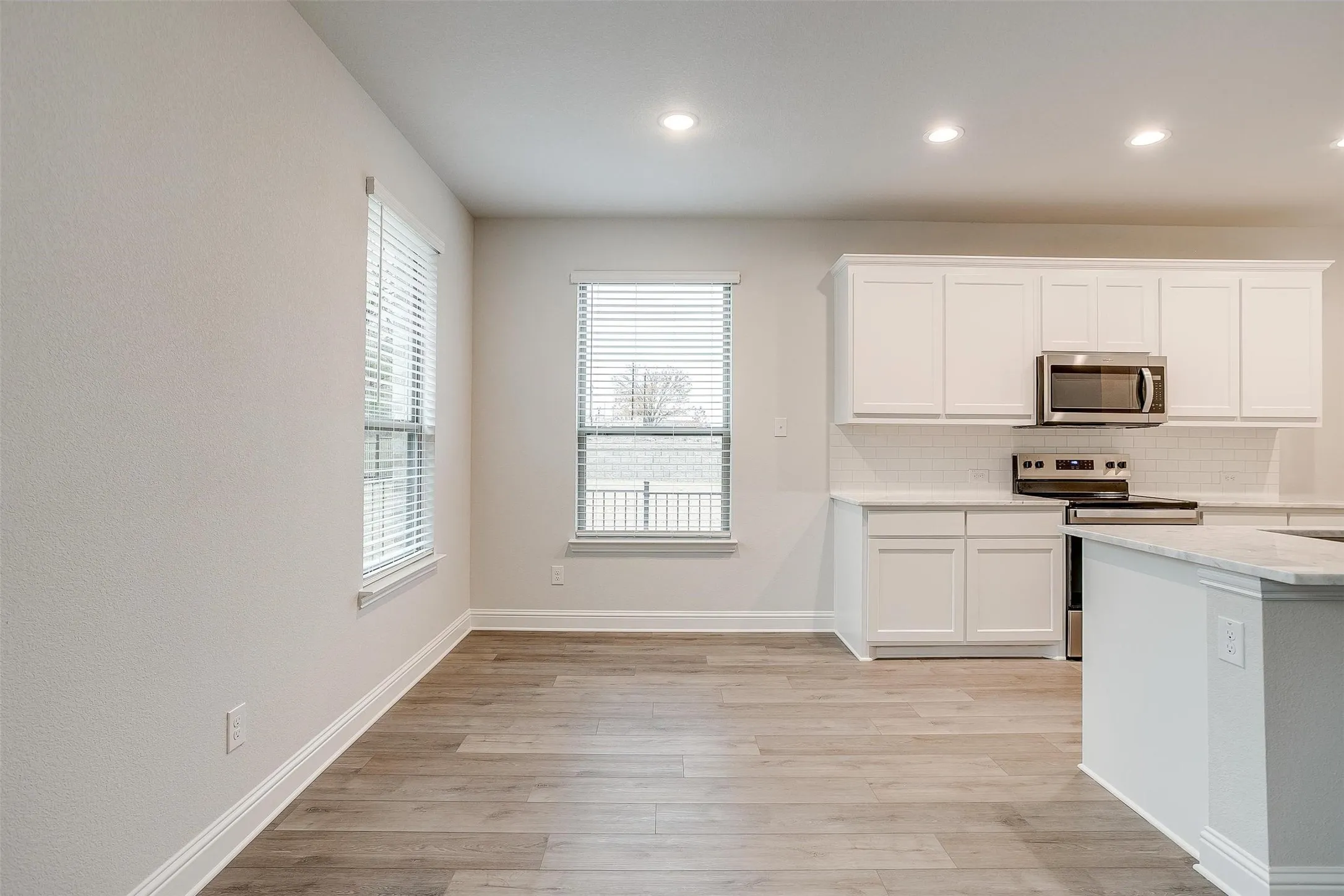 Open-concept space featuring wood-finish flooring, white cabinetry, stainless steel appliances, a subway tile backsplash, and recessed lighting