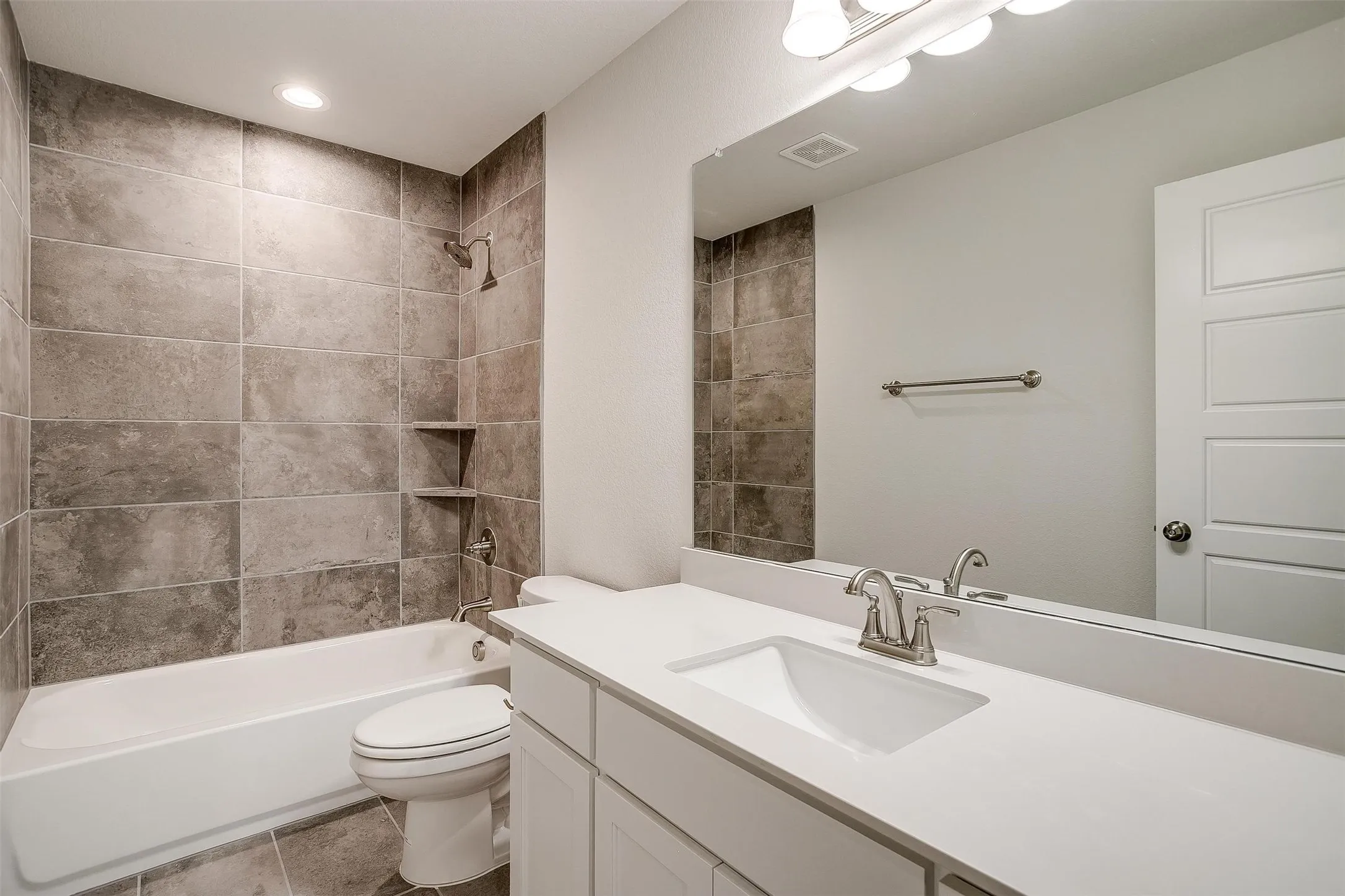 White vanity with an integrated sink, brushed nickel faucet, large mirror, and overhead vanity lighting