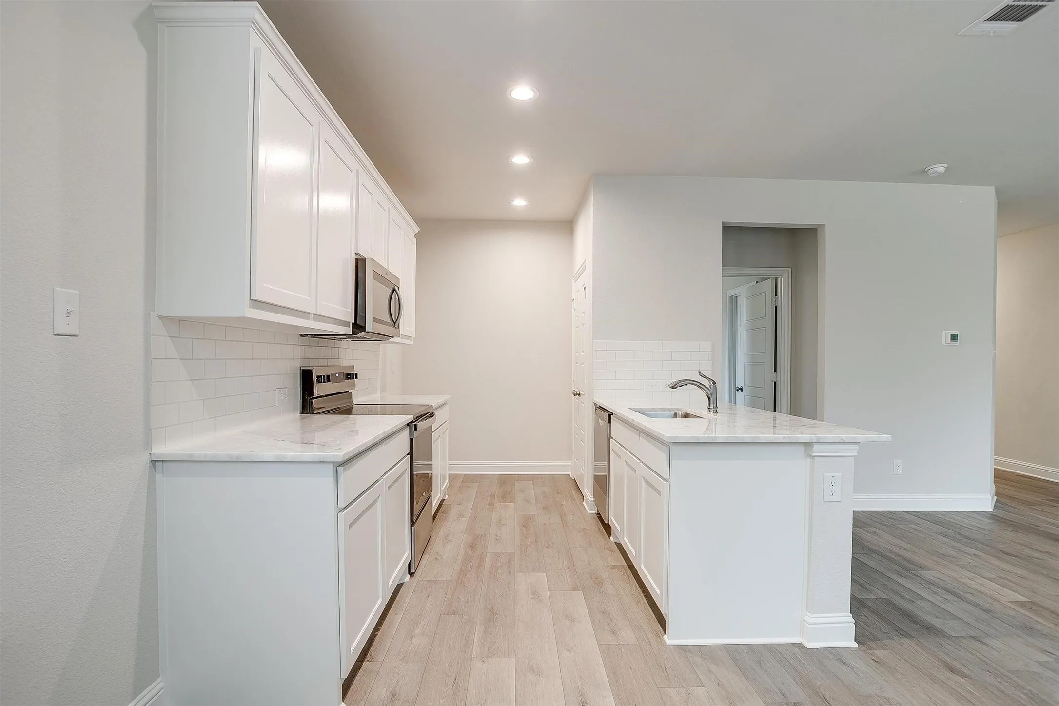Kitchen featuring wood-finish flooring, white cabinetry, a subway tile backsplash, and stainless steel appliances