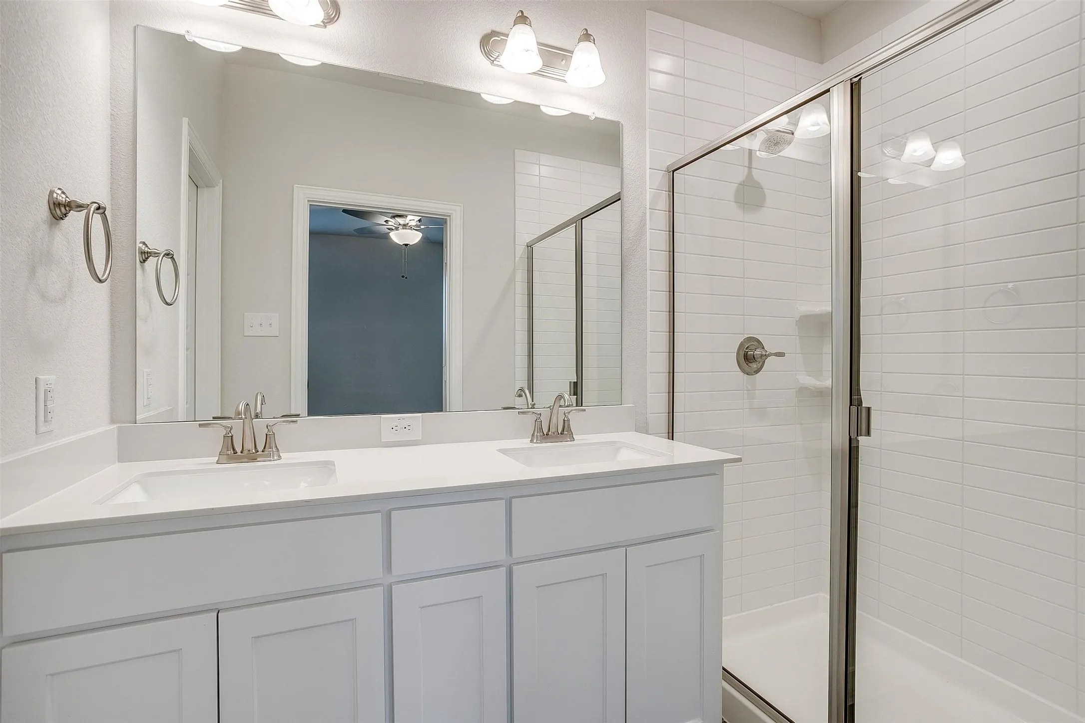 Dual vanity with white cabinetry and integrated sinks, brushed nickel fixtures, and a frameless shower enclosure