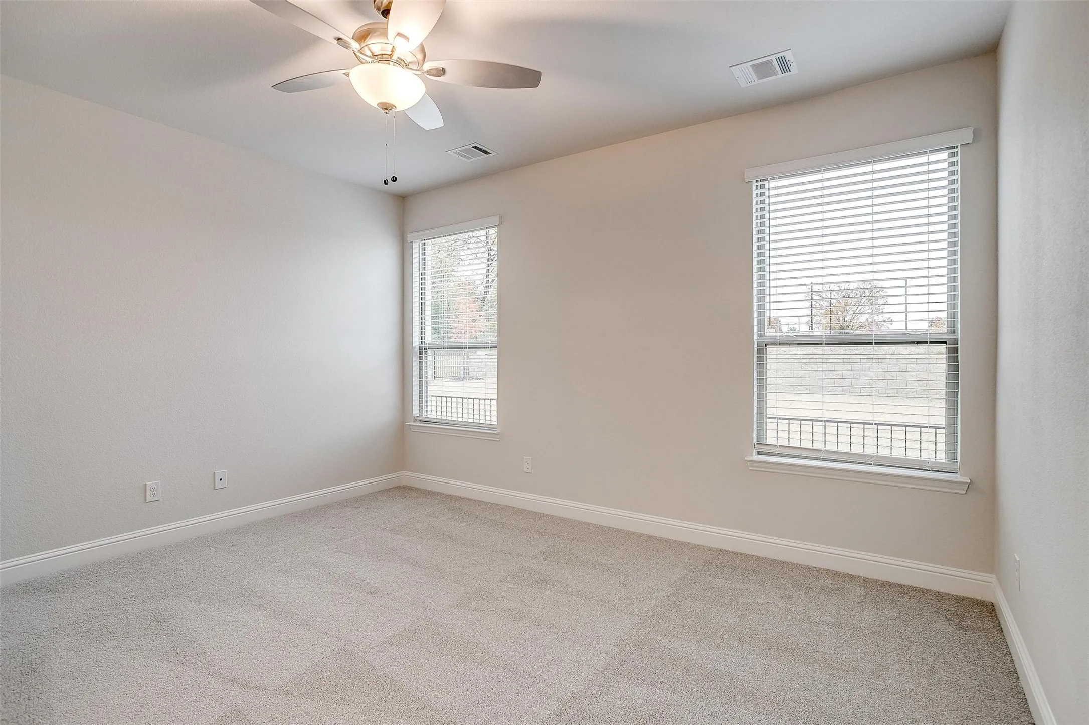 Neutral wall finishes, two windows with blinds, light-toned carpet flooring, and a ceiling fan with integrated lighting