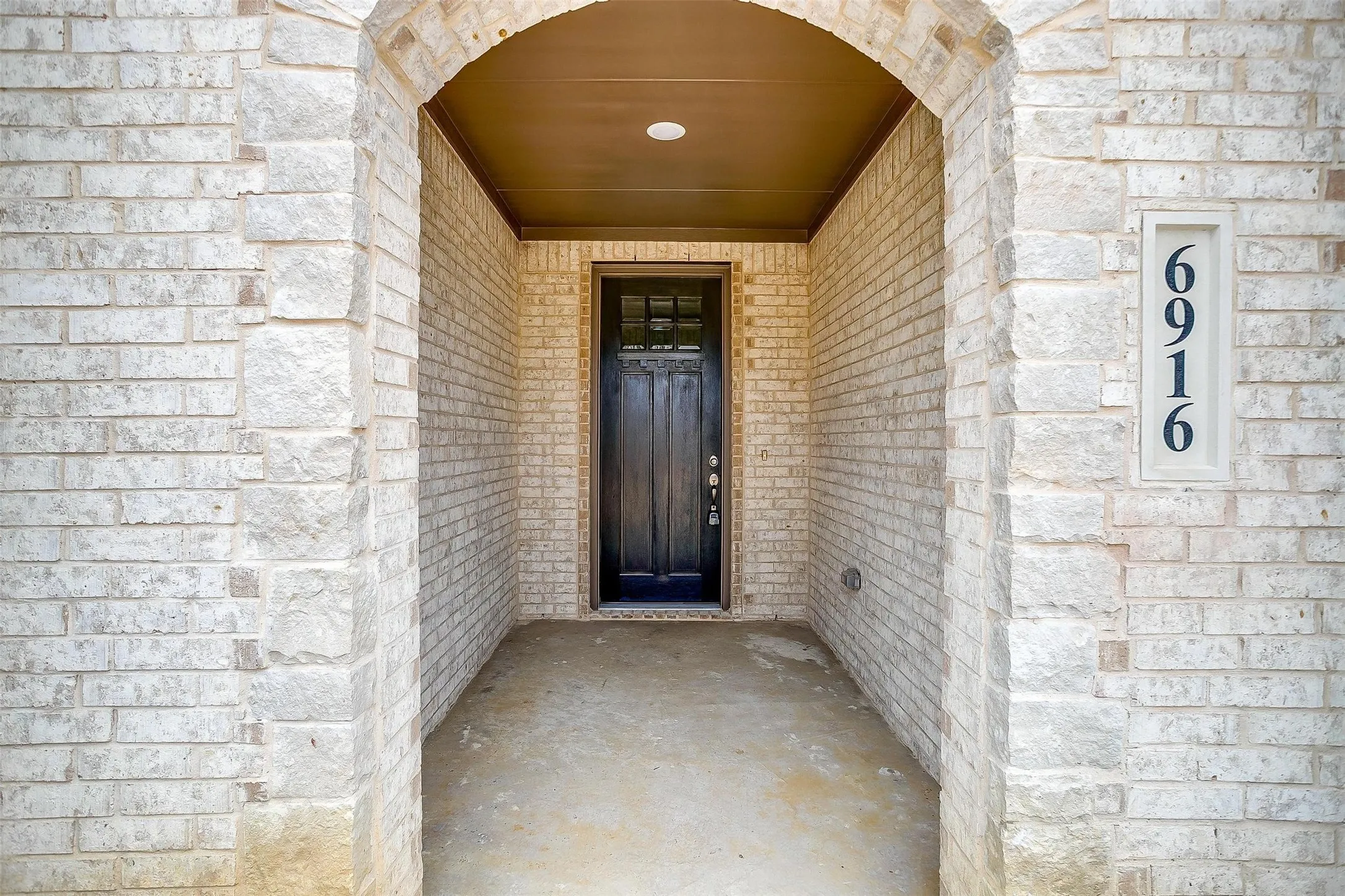 Arched entryway featuring light-toned brick, a dark wood-finish door with glass inserts, and recessed lighting