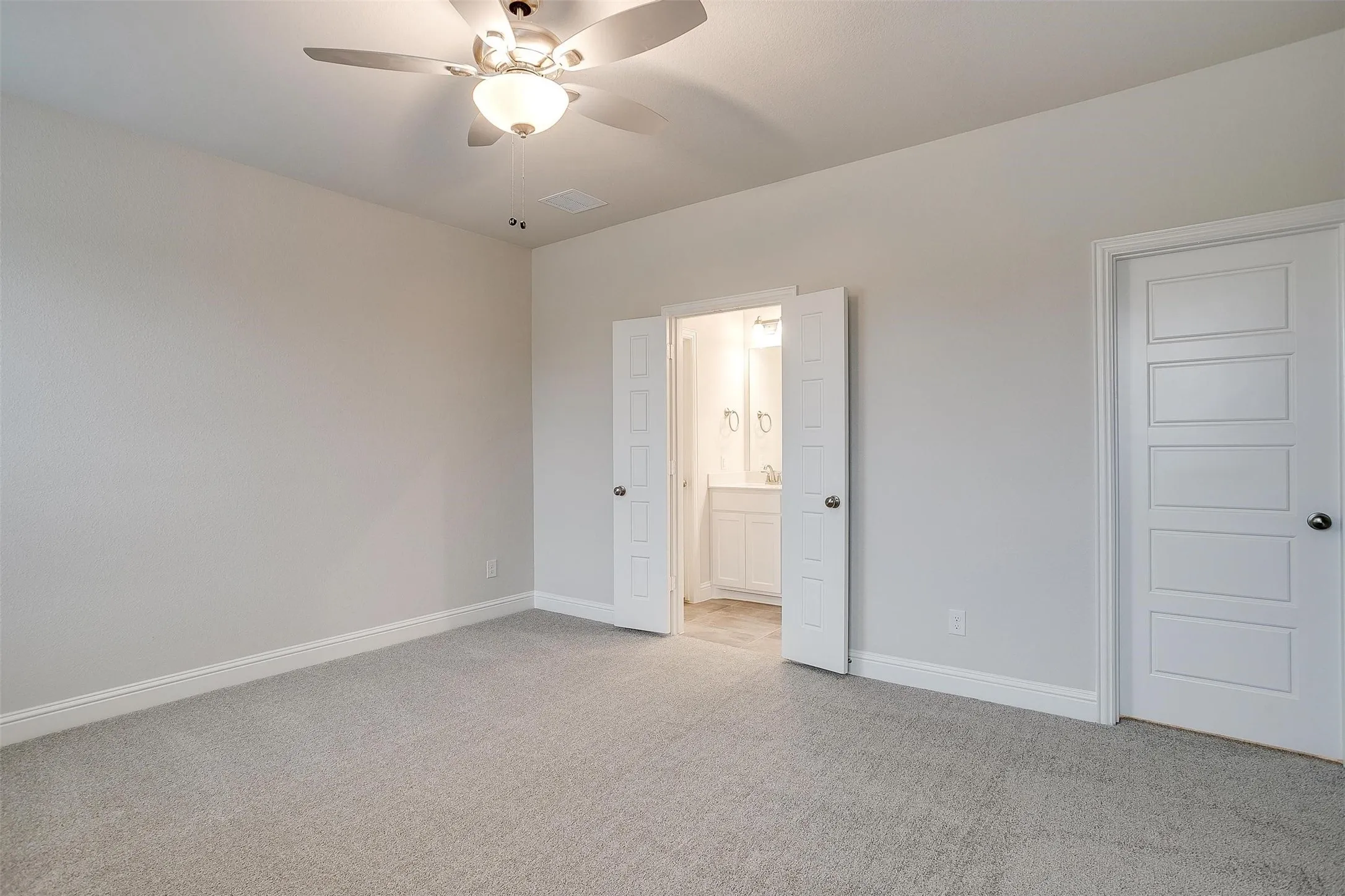 Carpeted room with ceiling fan and recessed lighting, featuring baseboards and a doorway to a bathroom with a vanity