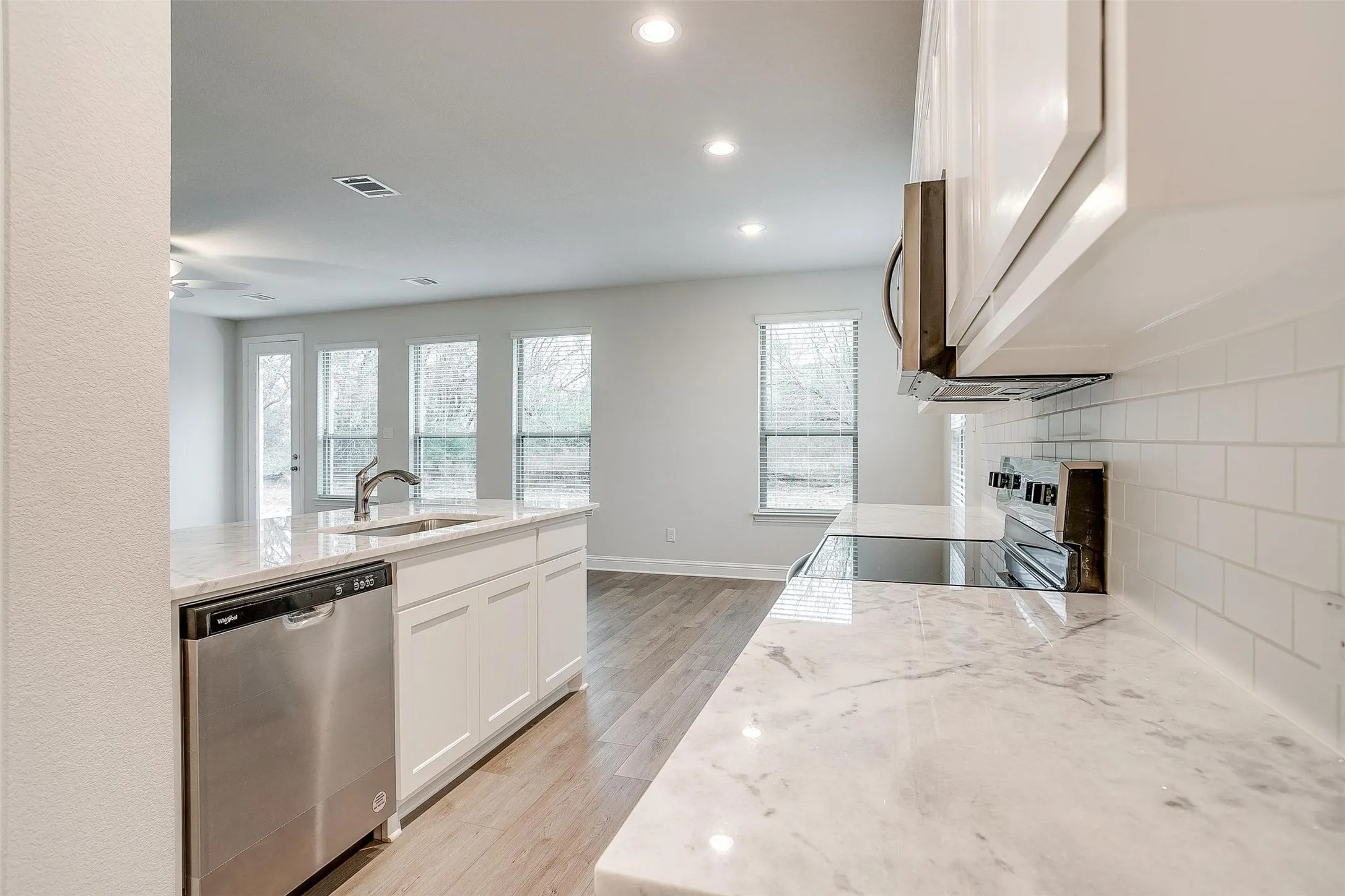 Kitchen featuring white cabinetry, light-toned countertops, white subway tile backsplash, and stainless steel appliances