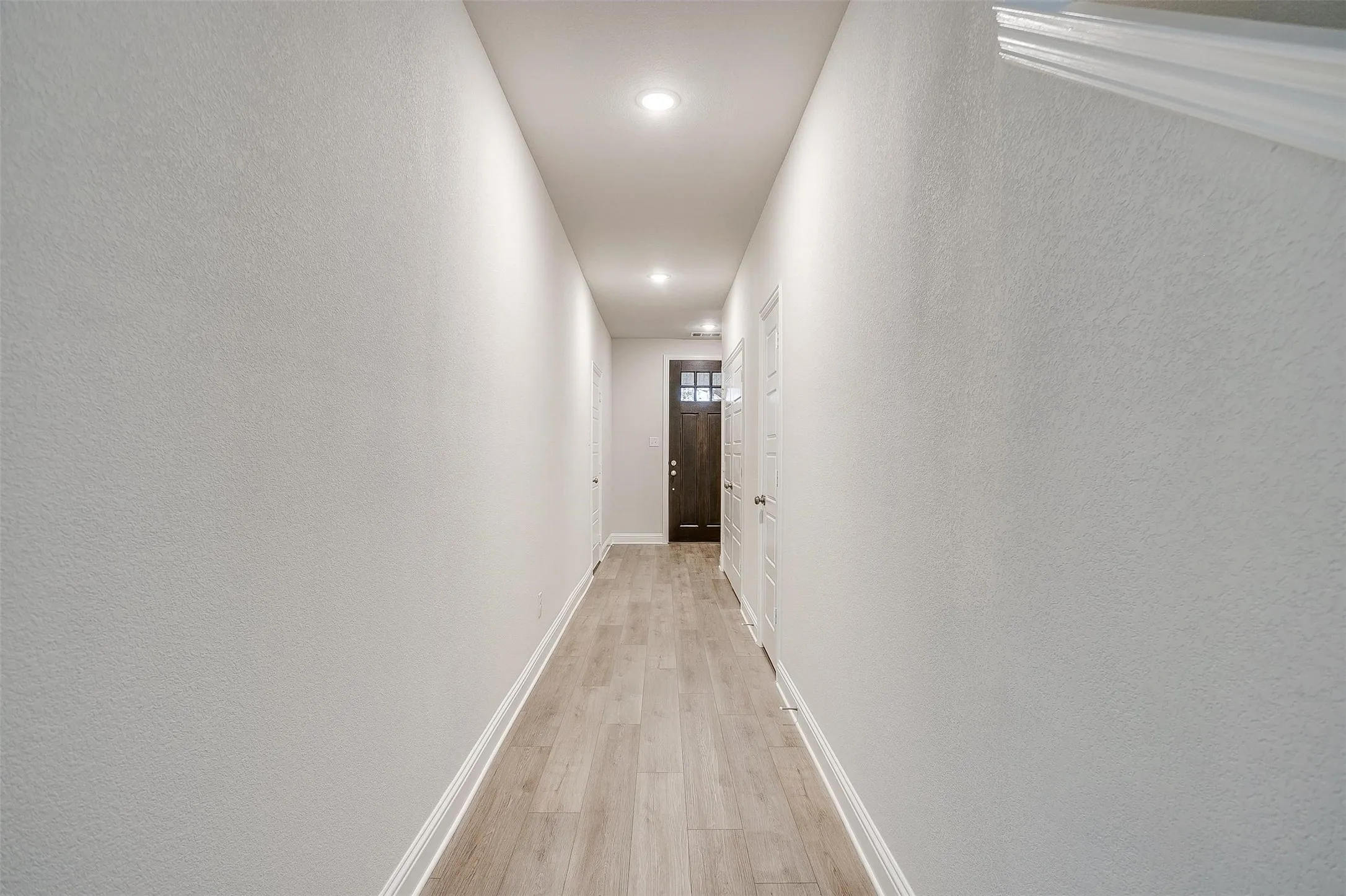 Recessed ceiling lighting, wood-finish flooring, white baseboards, and a dark wood-finish entry door with glass panels